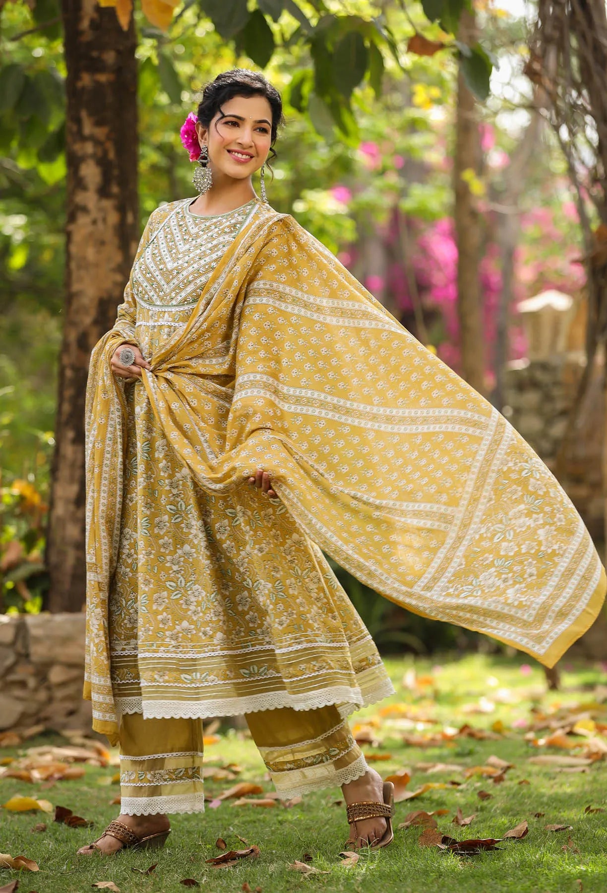 Woman in a yellow and white traditional outfit standing outdoors with greenery in the background