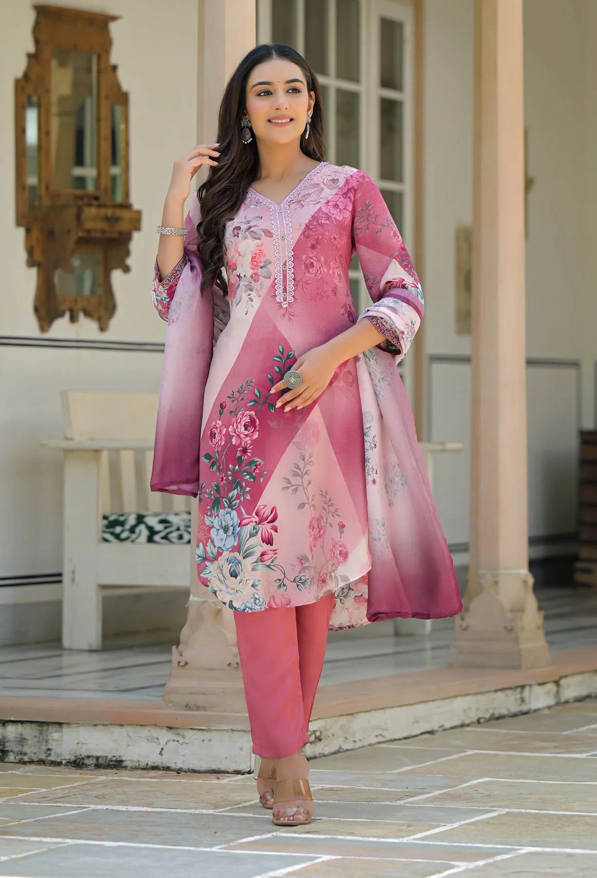 Woman in a pink traditional outfit with floral patterns standing in front of a building.