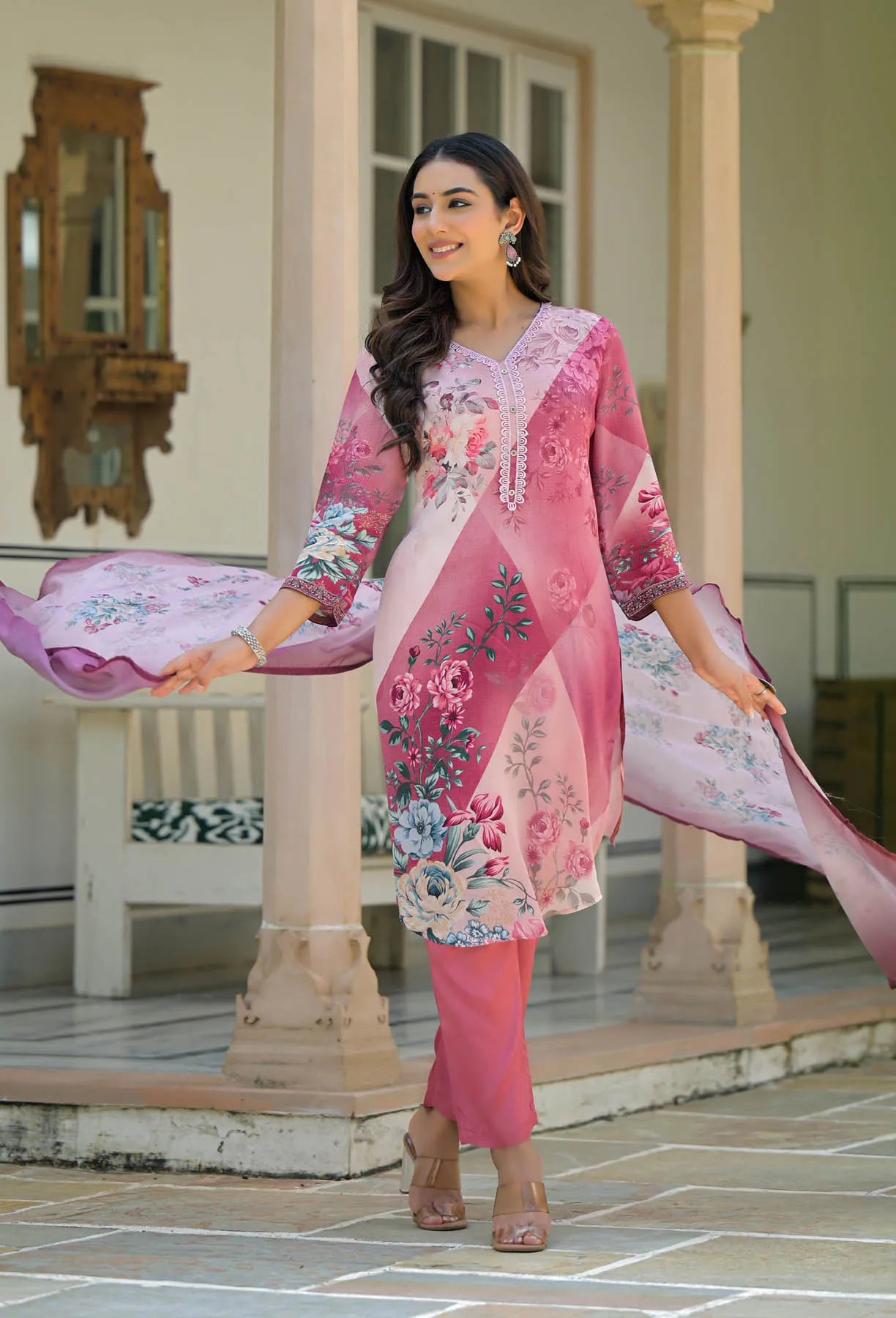 Woman in a pink embroidered outfit standing on a stone patio.