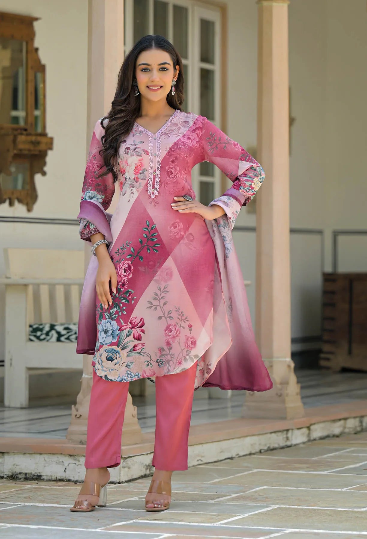 Woman wearing a pink traditional outfit with floral patterns in an outdoor setting.