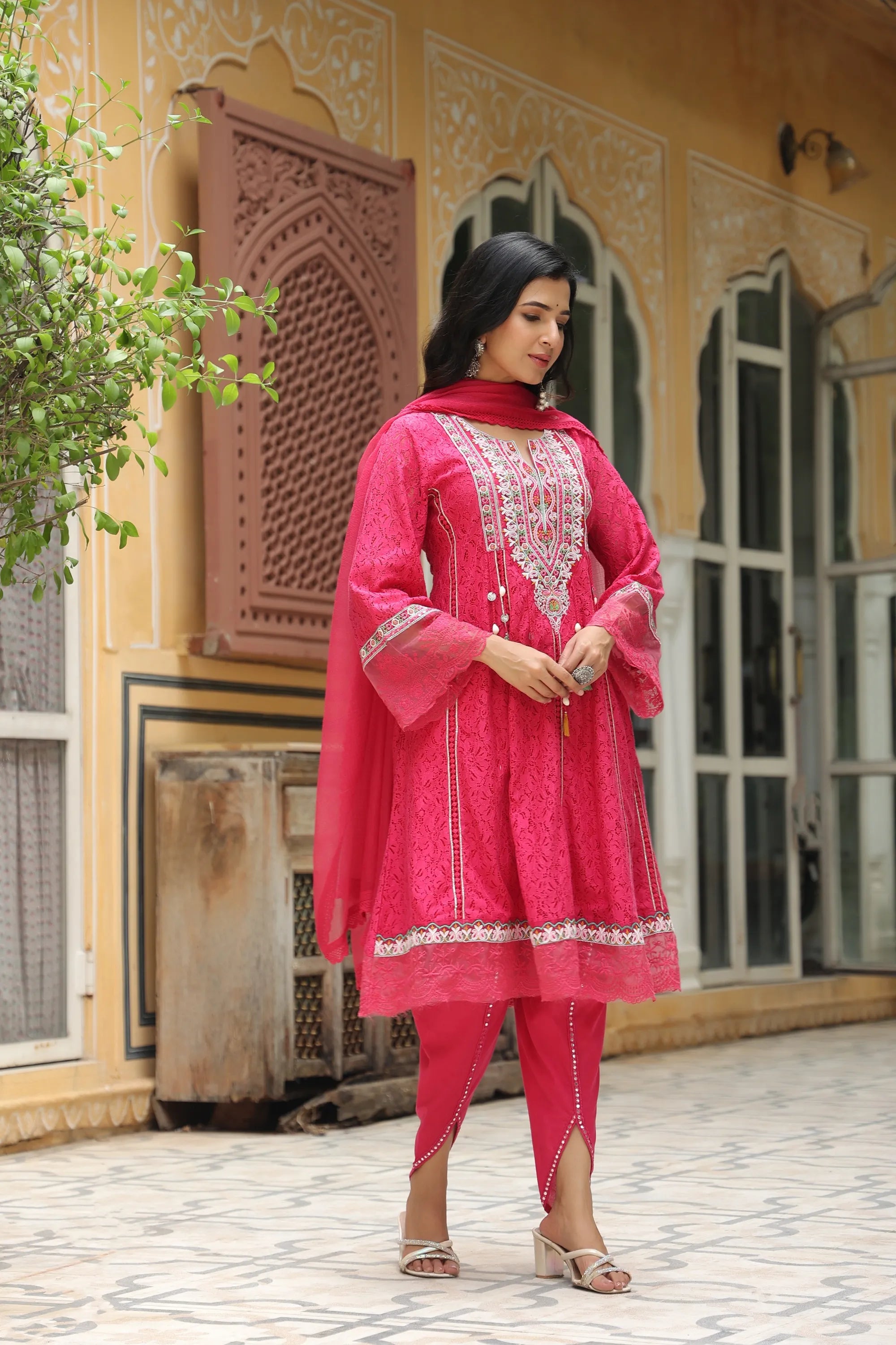 Woman in a bright pink traditional outfit standing in front of a decorative building.