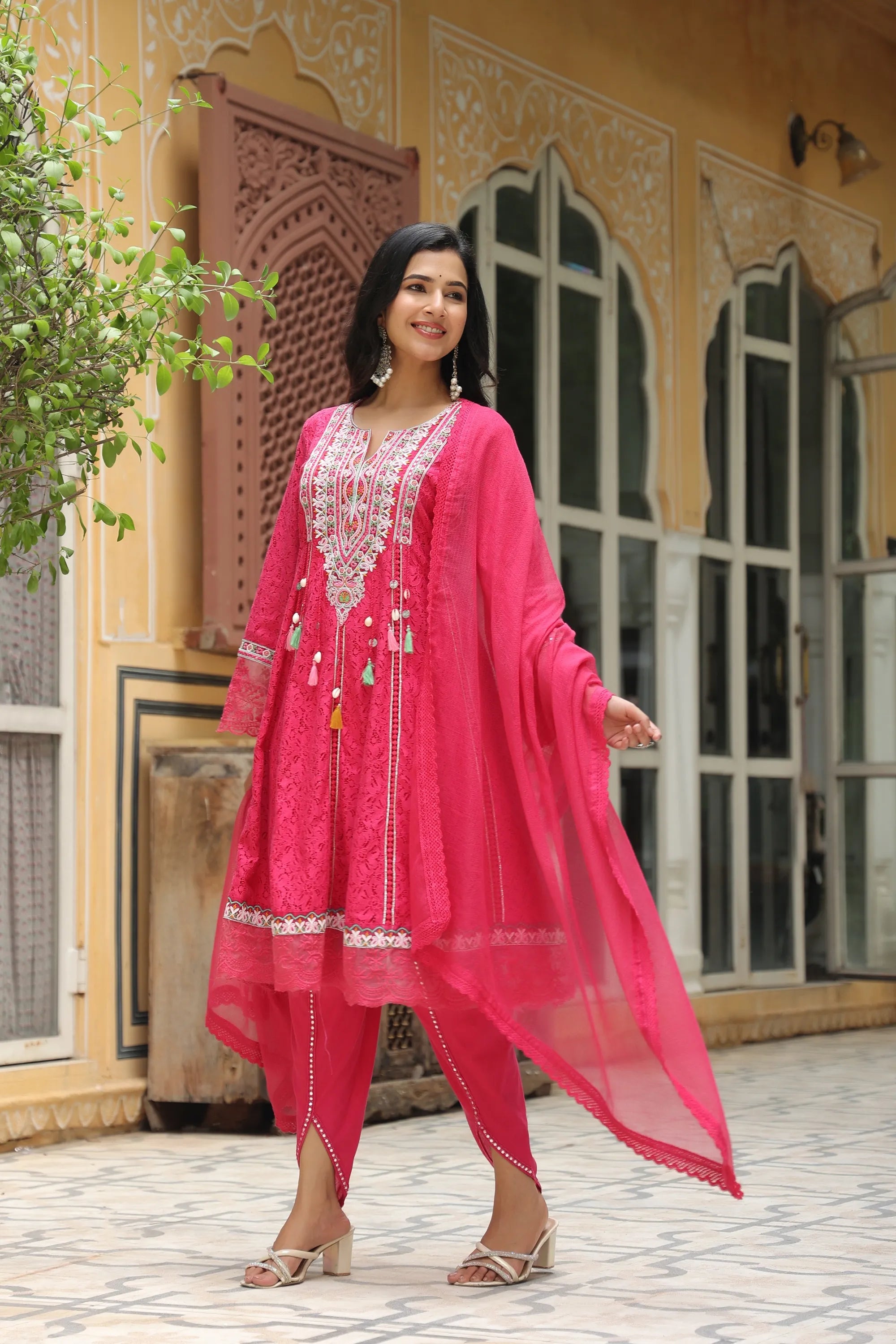 Woman in a pink traditional outfit standing in front of a decorative building.