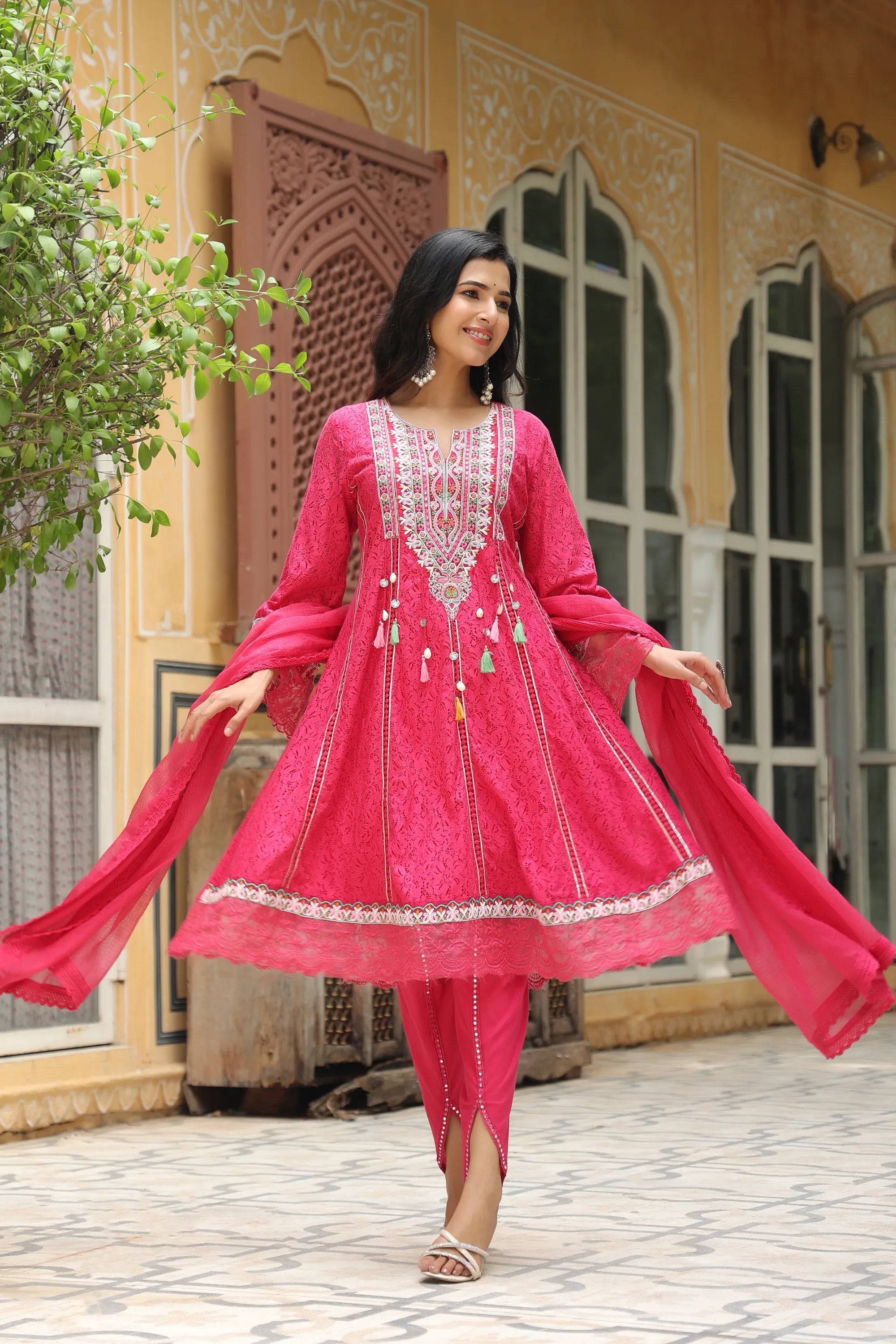 Woman in a pink traditional outfit standing in front of a decorative building.