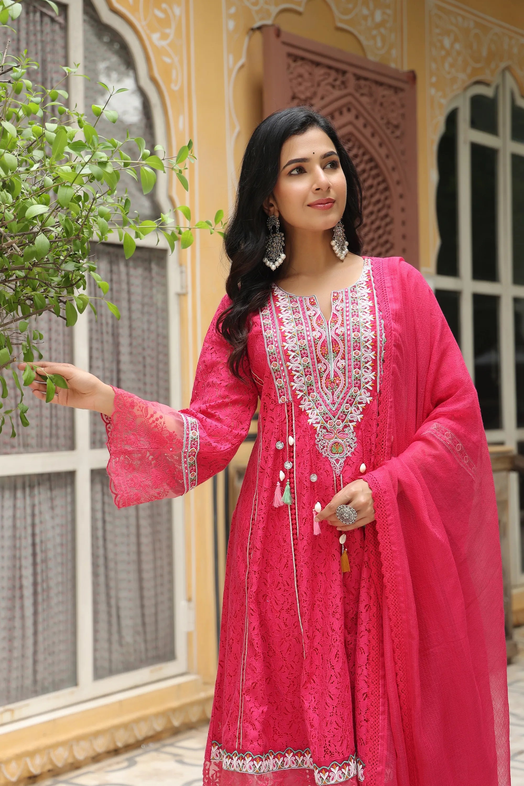 Woman in a pink embroidered traditional outfit standing outdoors.