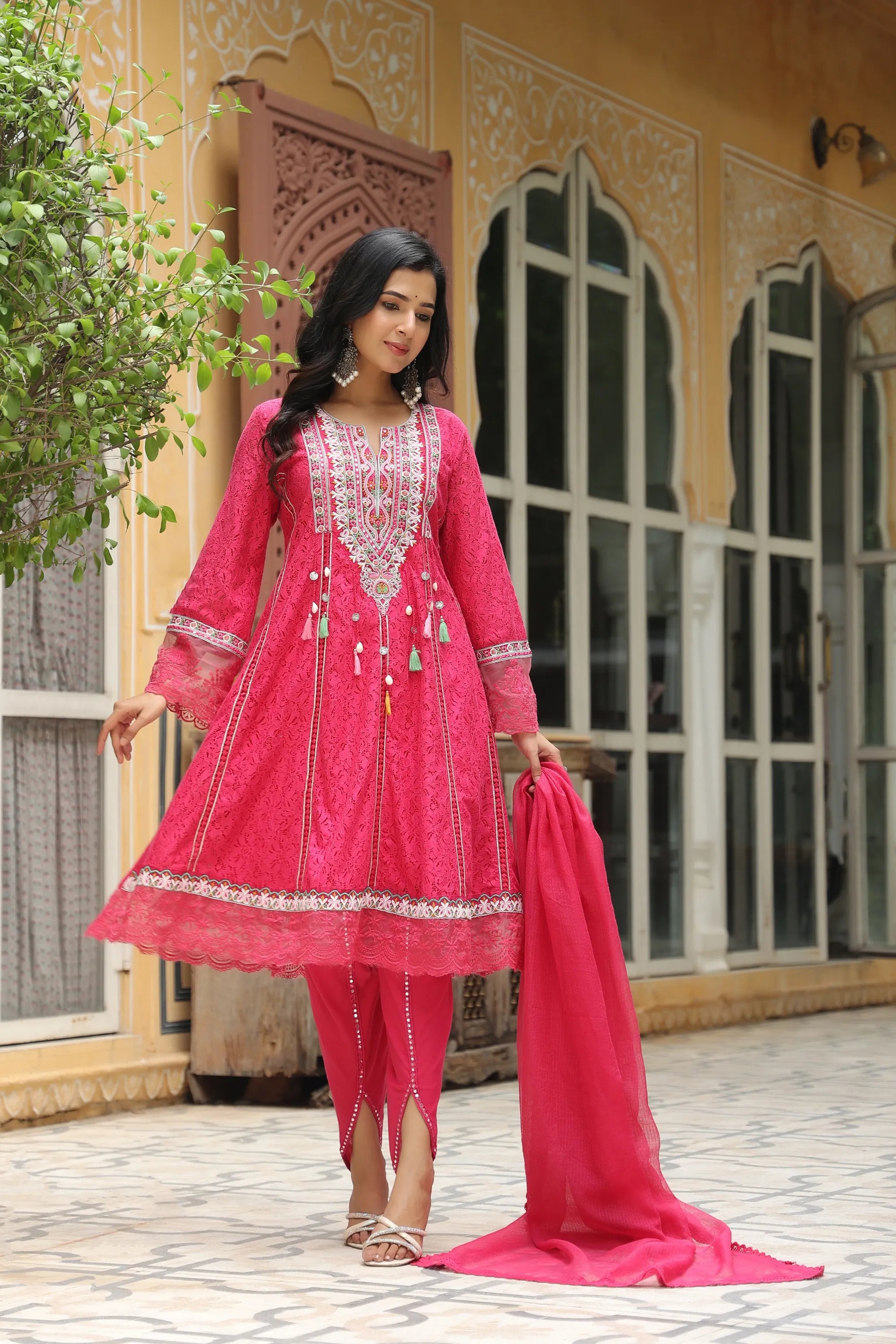 Woman in a pink traditional outfit standing in front of a decorative building.