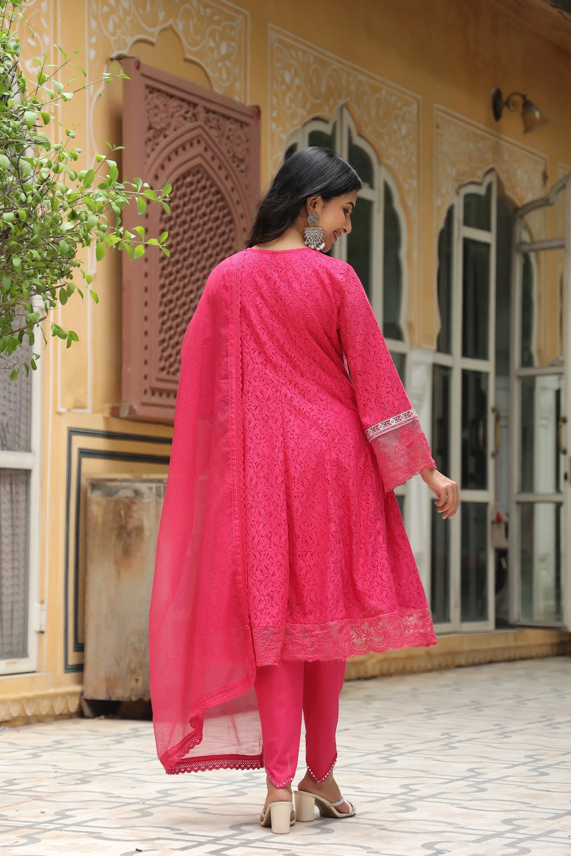 Woman in a bright pink traditional outfit standing in front of a decorative building.