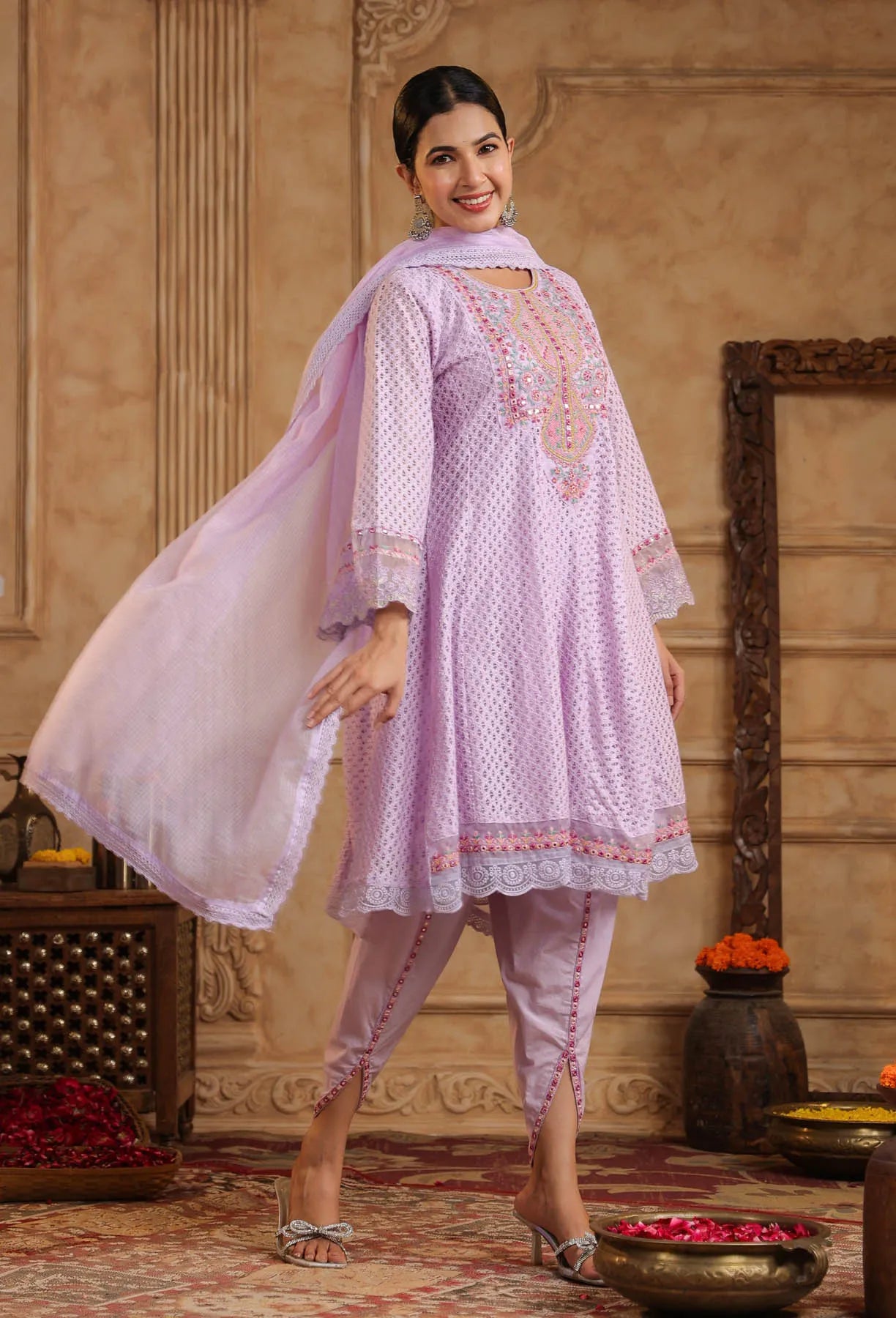 Woman wearing a light pink traditional outfit with embroidery in an ornate room.