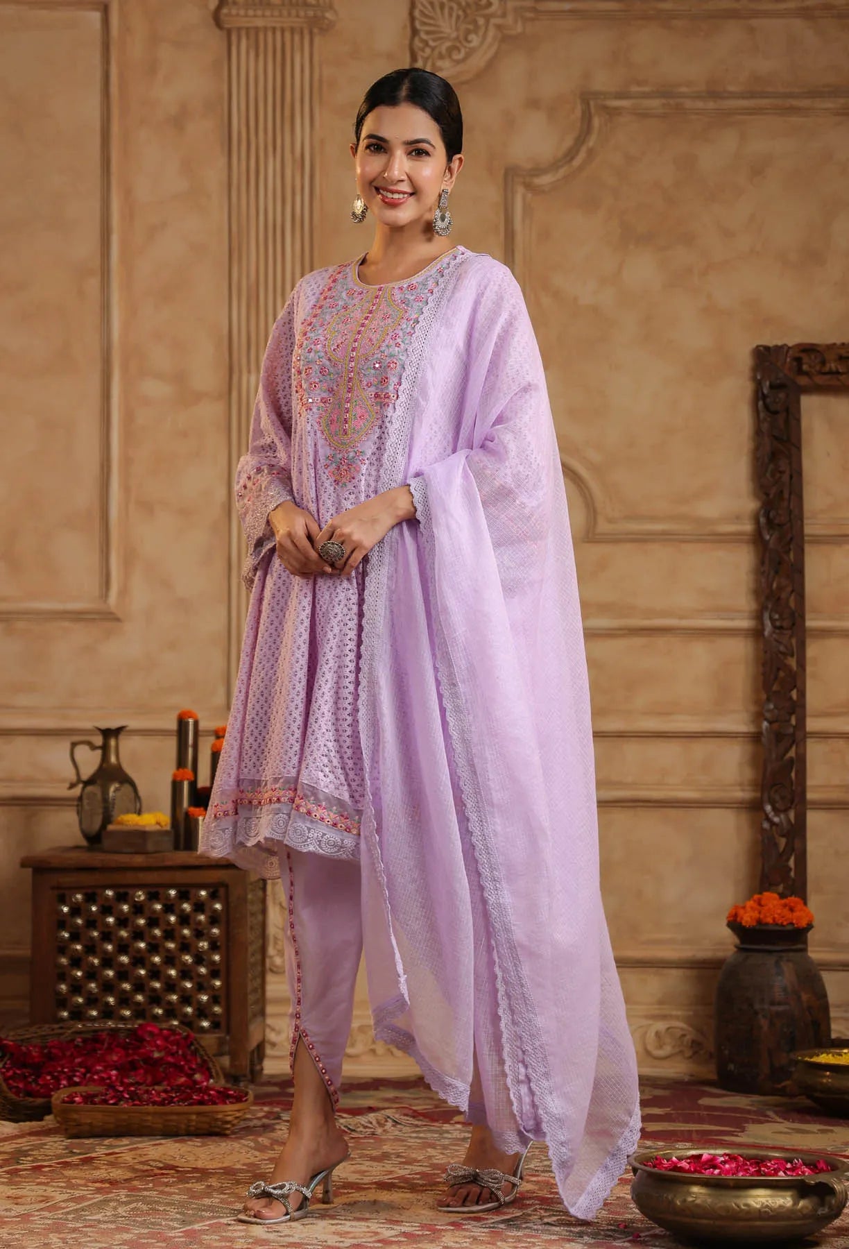 Woman in a light purple traditional outfit standing in an ornate room.