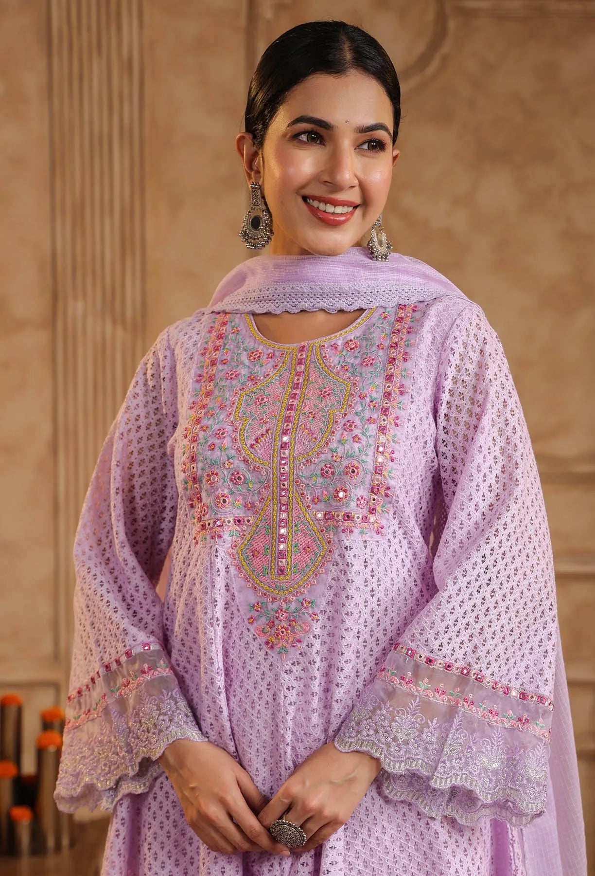 Woman wearing a light purple embroidered traditional outfit with a beige background