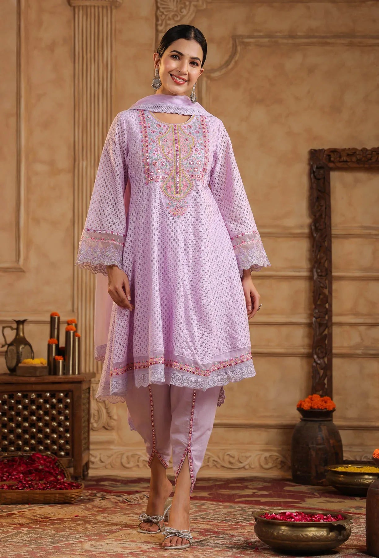 Woman wearing a light pink embroidered traditional outfit in an ornate room.