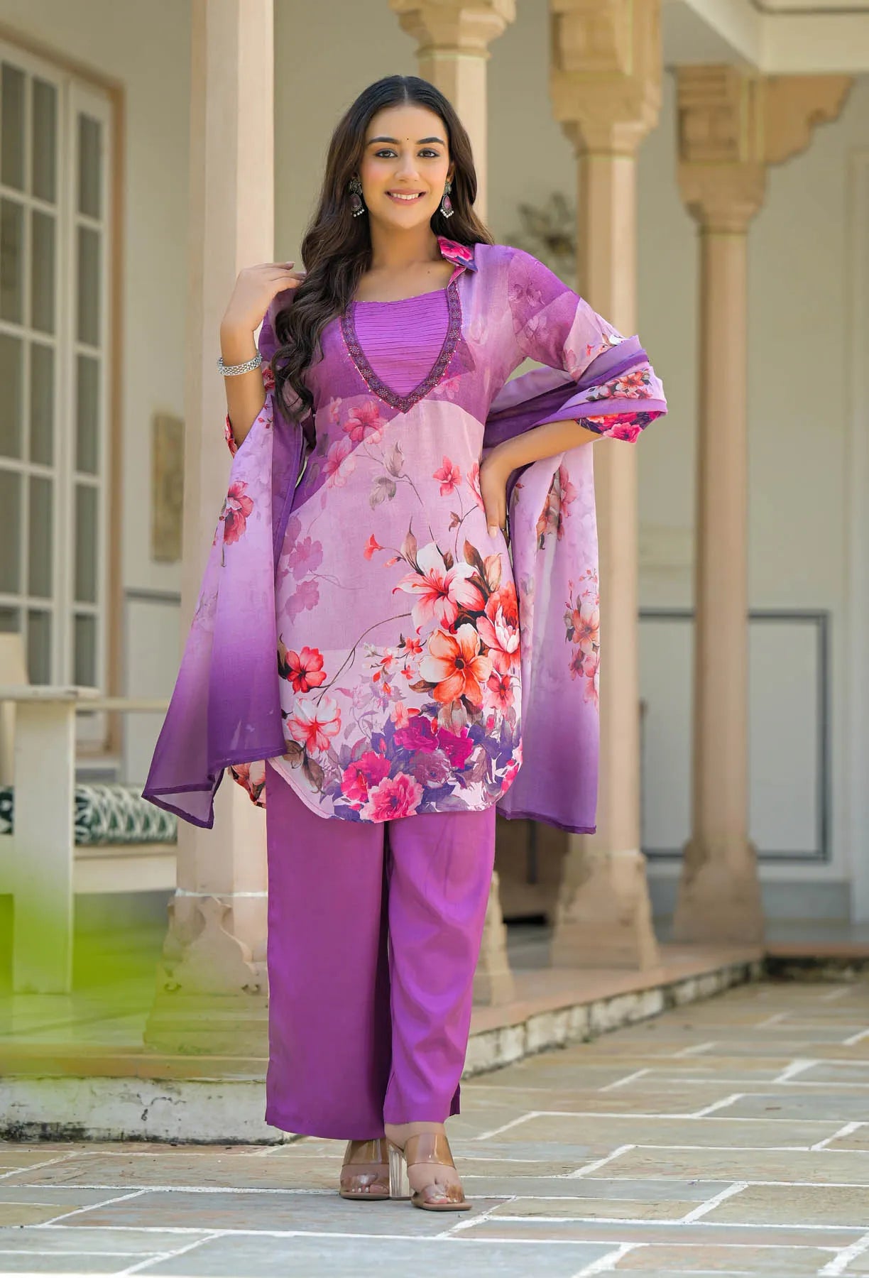 Woman in a purple floral outfit standing in front of a building with columns.