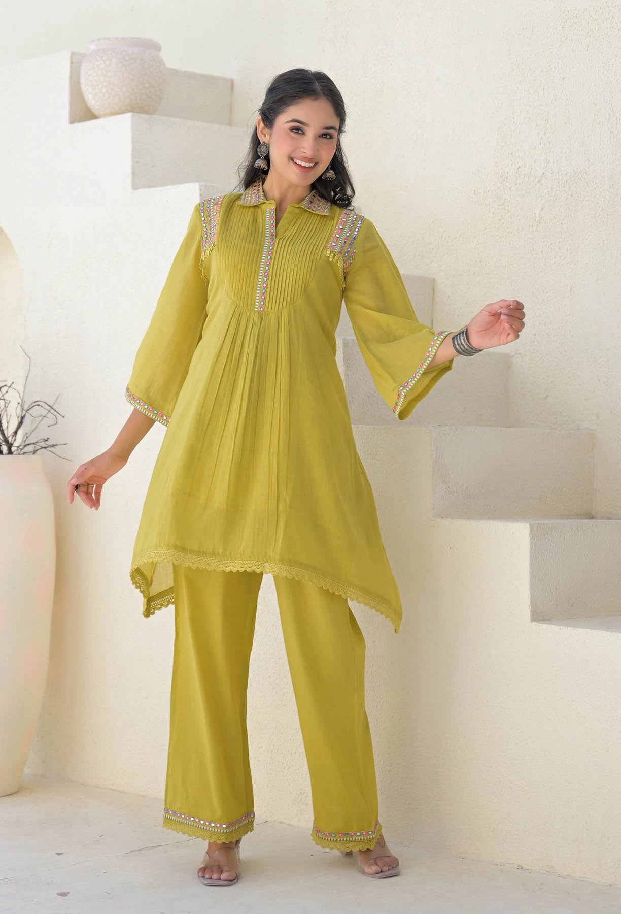 Woman wearing a yellow traditional outfit with intricate designs in a minimalistic setting.