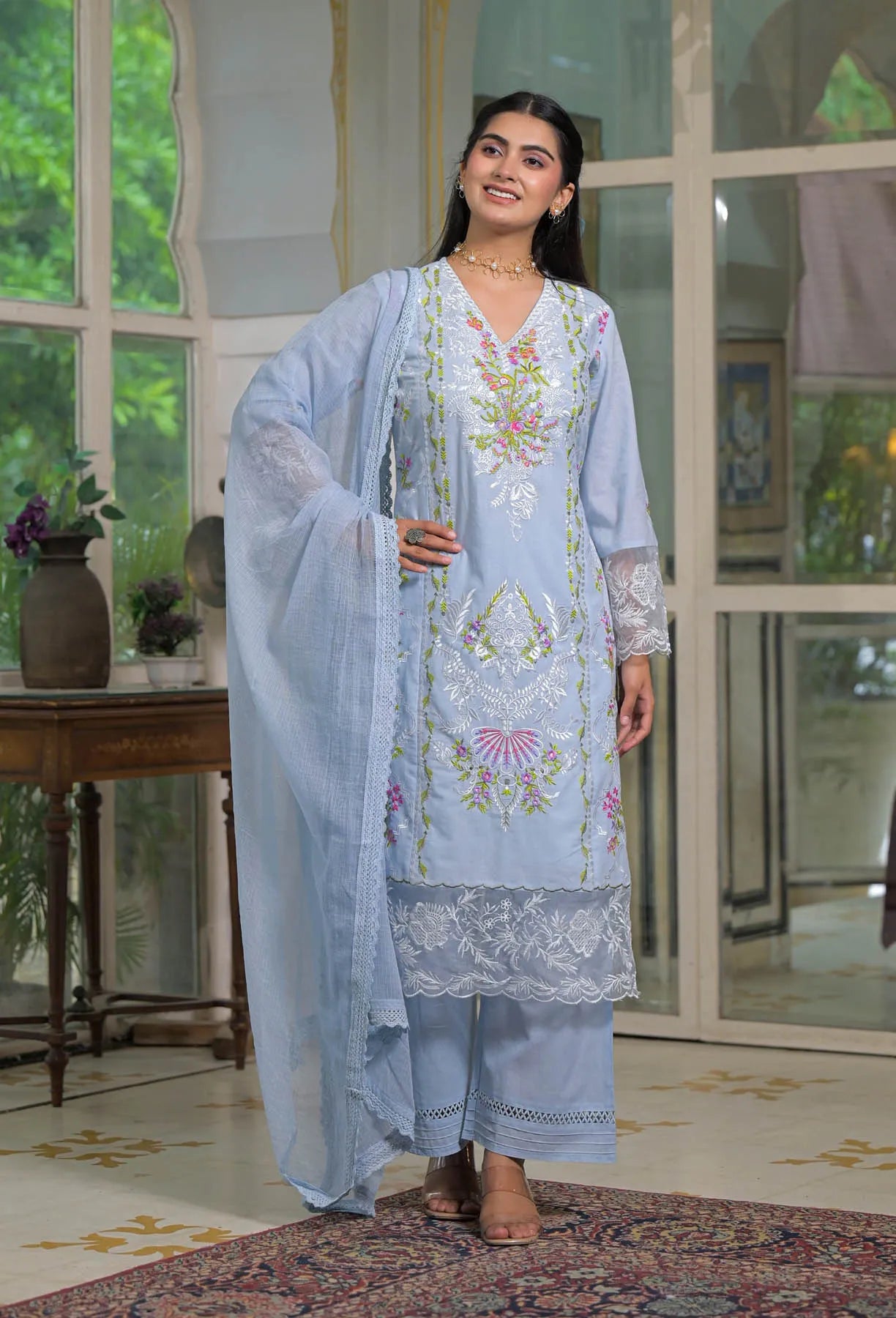 Woman wearing a light blue embroidered traditional outfit indoors.