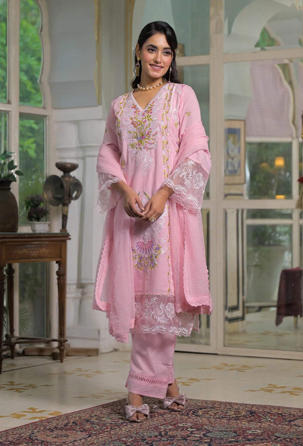 Woman in a pink traditional outfit standing in a decorated room.