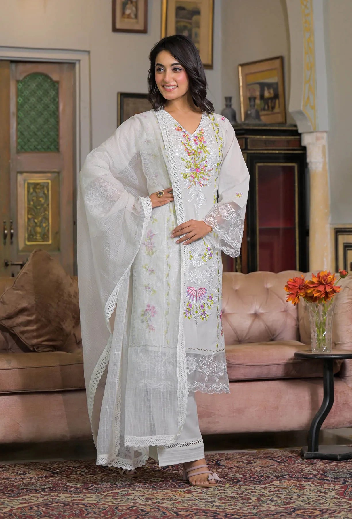 Woman in a white embroidered traditional outfit standing in a living room.