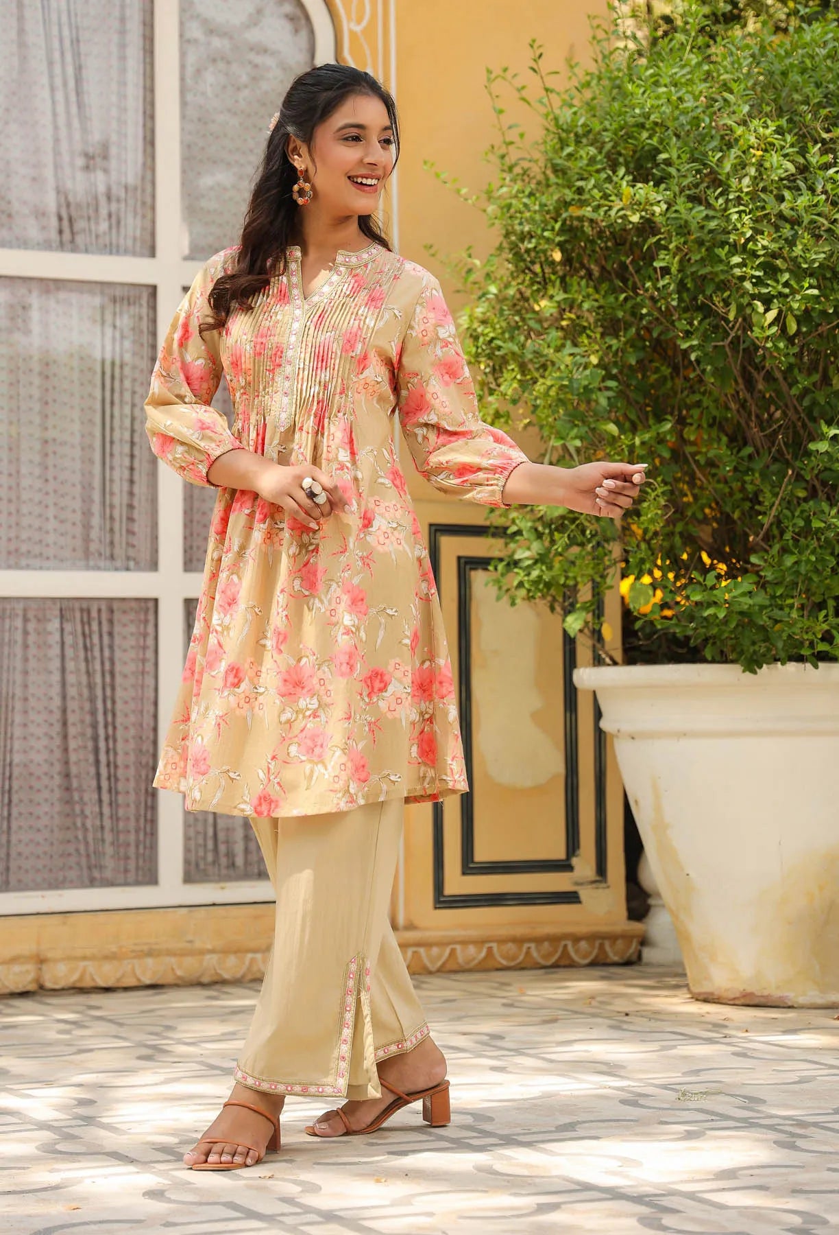 Woman in a floral kurta with beige pants standing outdoors.