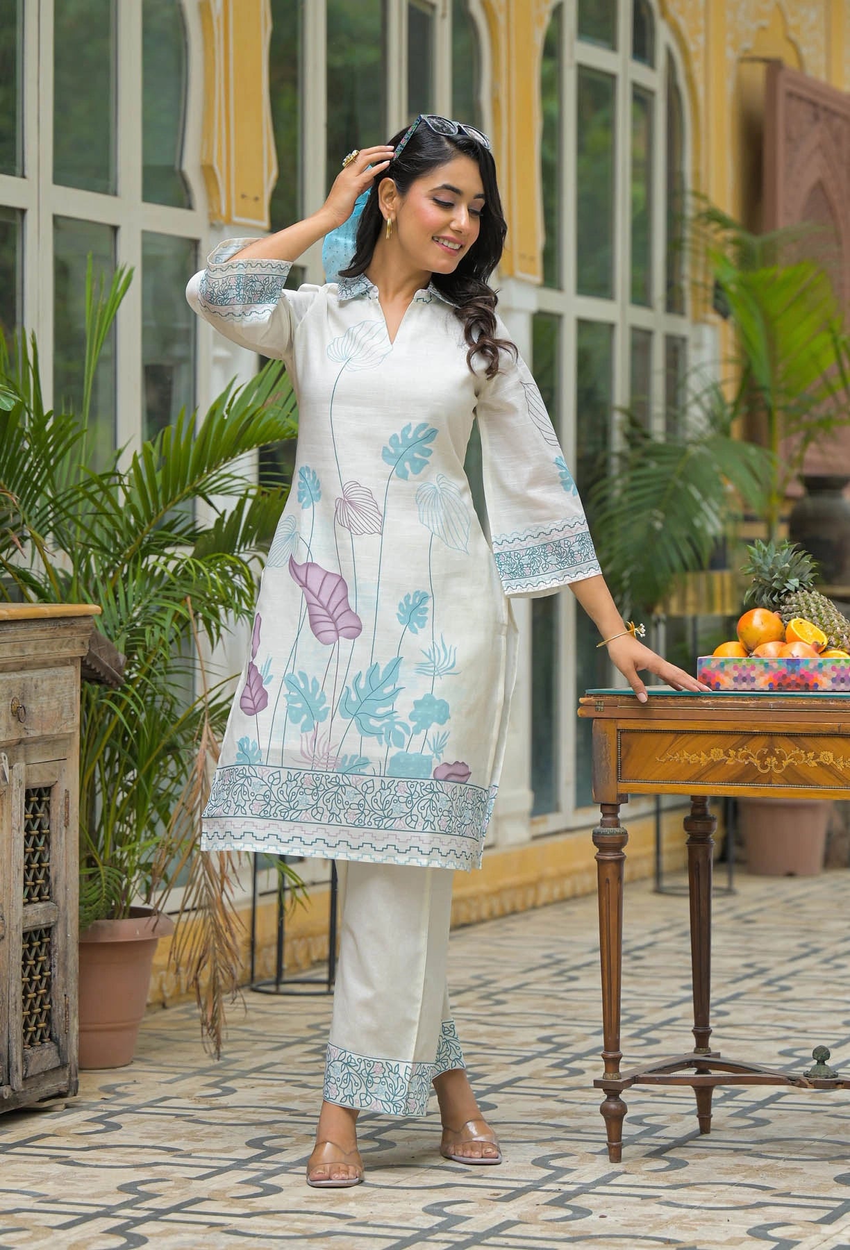 Woman in a white traditional outfit with floral patterns standing in an outdoor setting.
