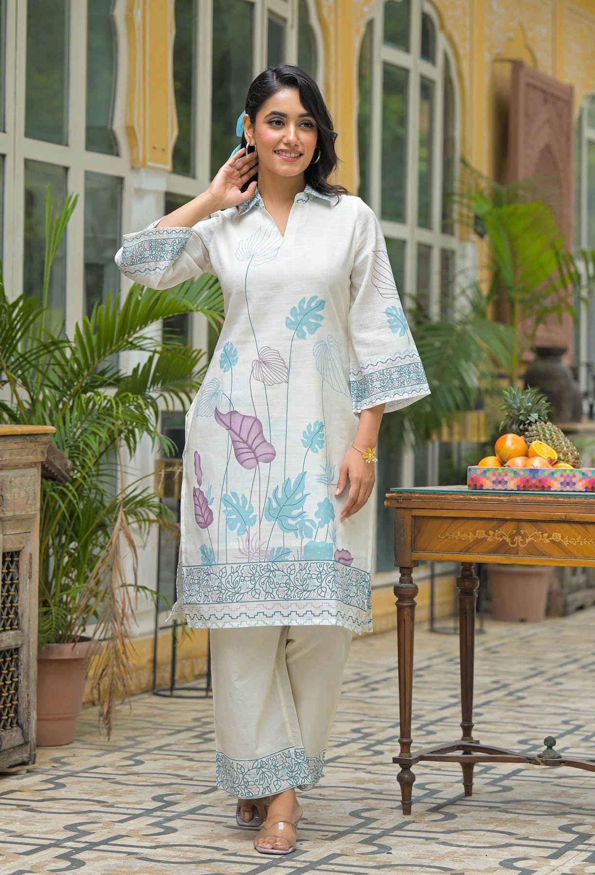 Woman in a floral dress standing outdoors with plants and a table in the background