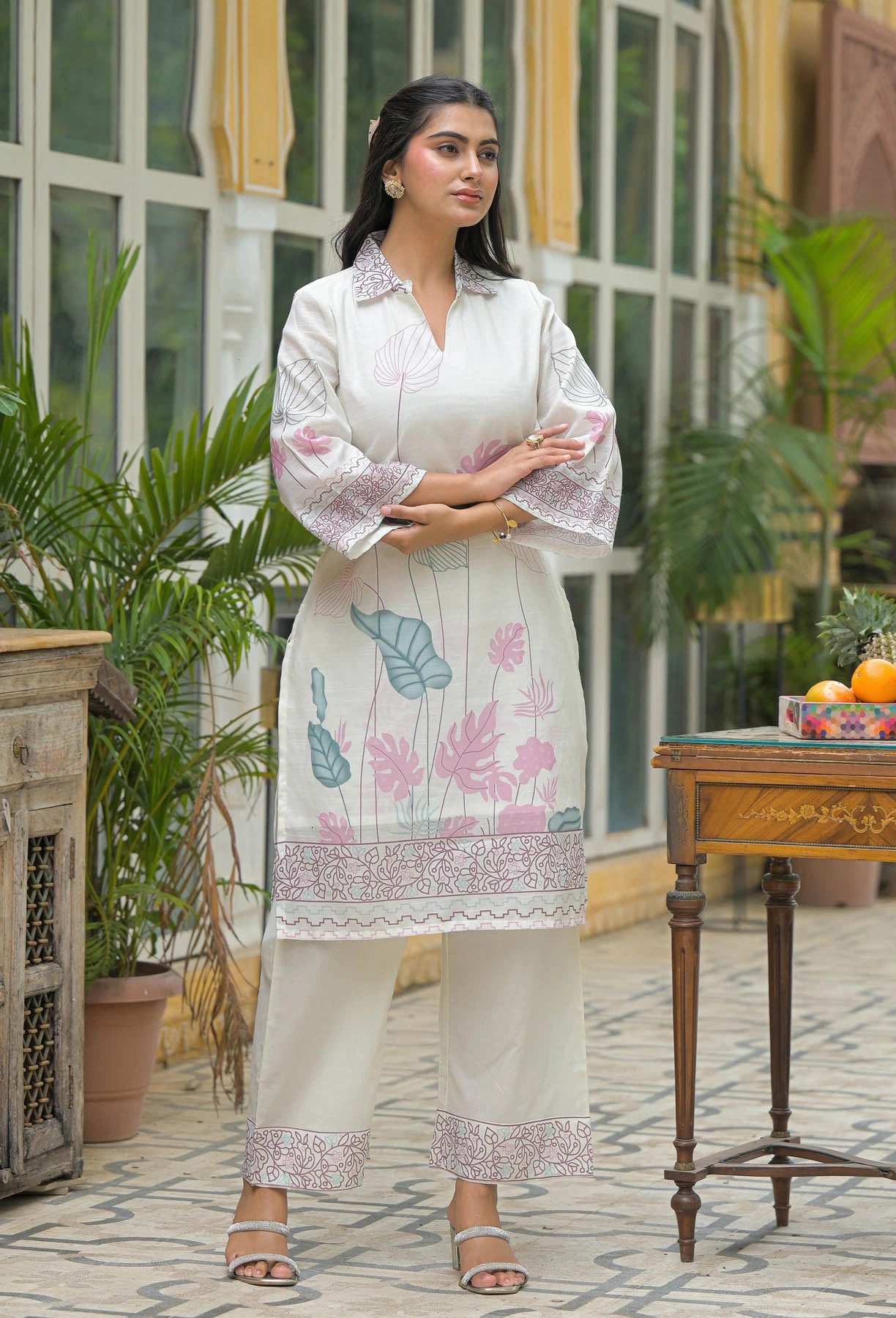 Woman in a floral dress standing in an outdoor setting with plants and a table.