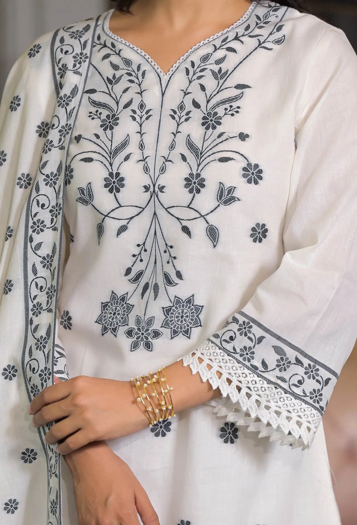 White garment with black floral embroidery and lace details, worn by a person.
