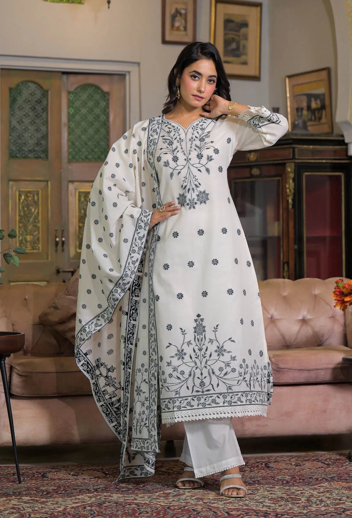 Woman in a white embroidered traditional outfit standing in a living room.