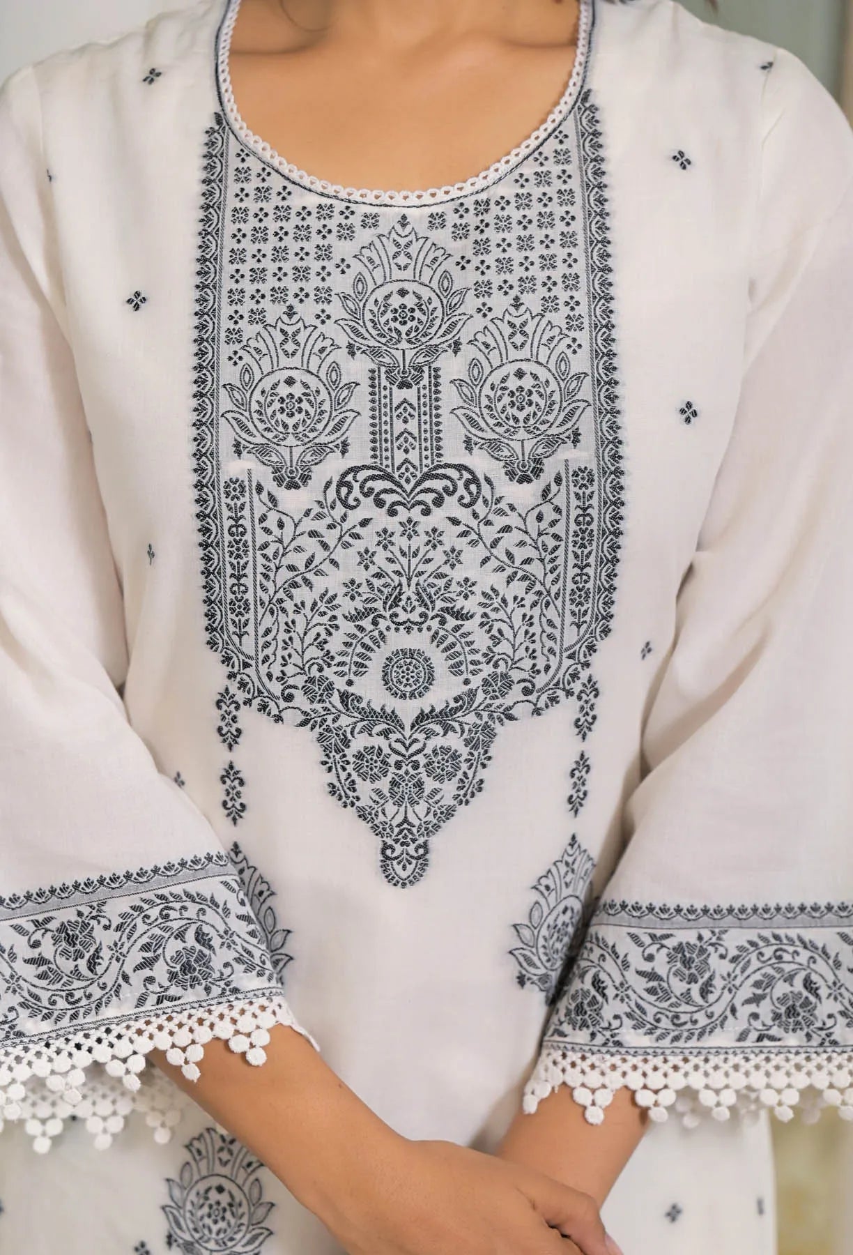 White garment with black intricate embroidery on a neutral background