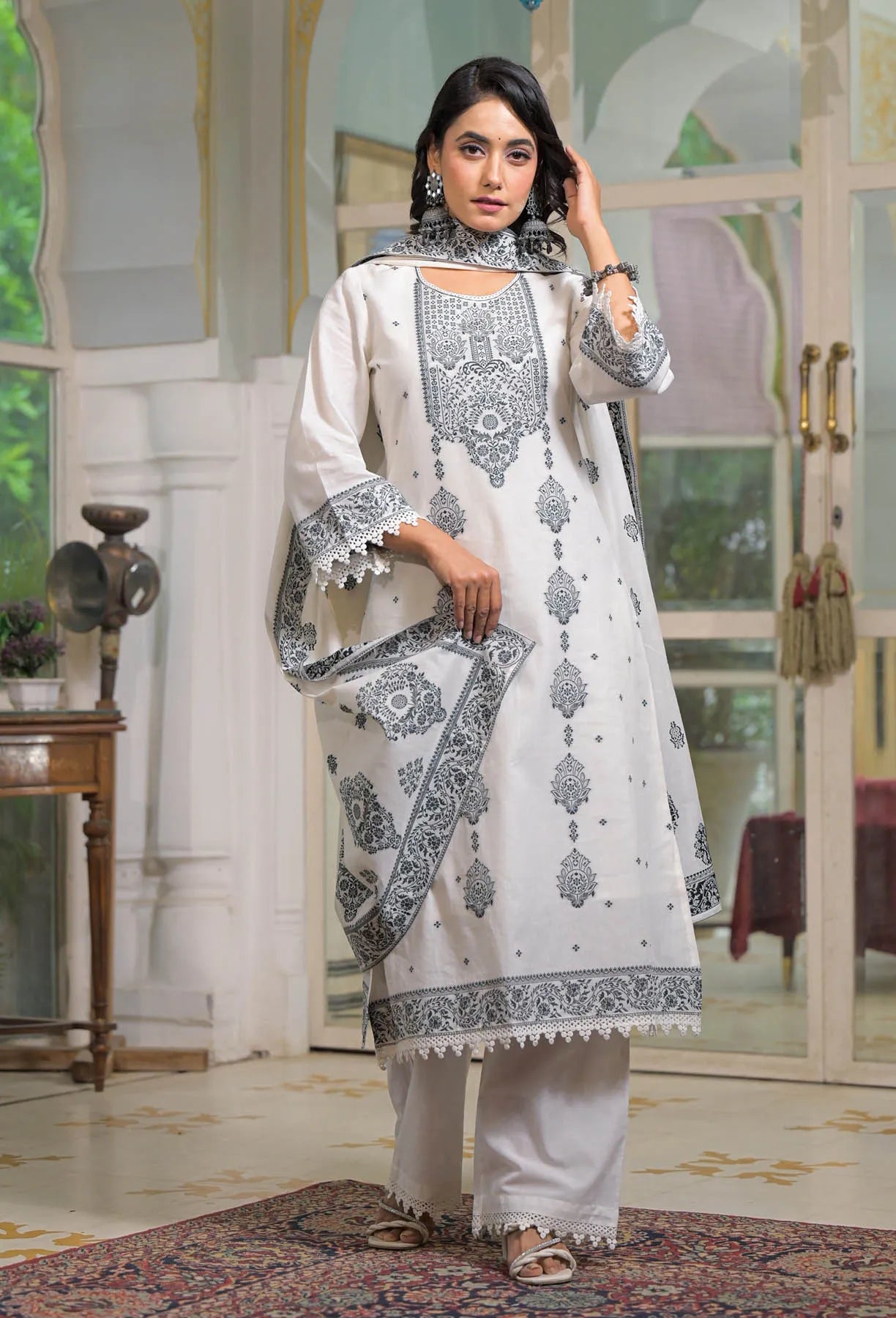 Woman wearing a white and gray embroidered traditional outfit in an elegant room.