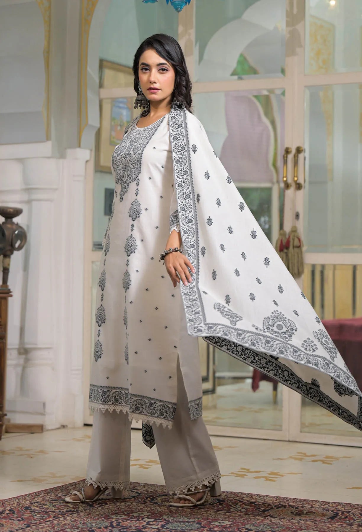 Woman in a white traditional outfit with black patterns in an indoor setting