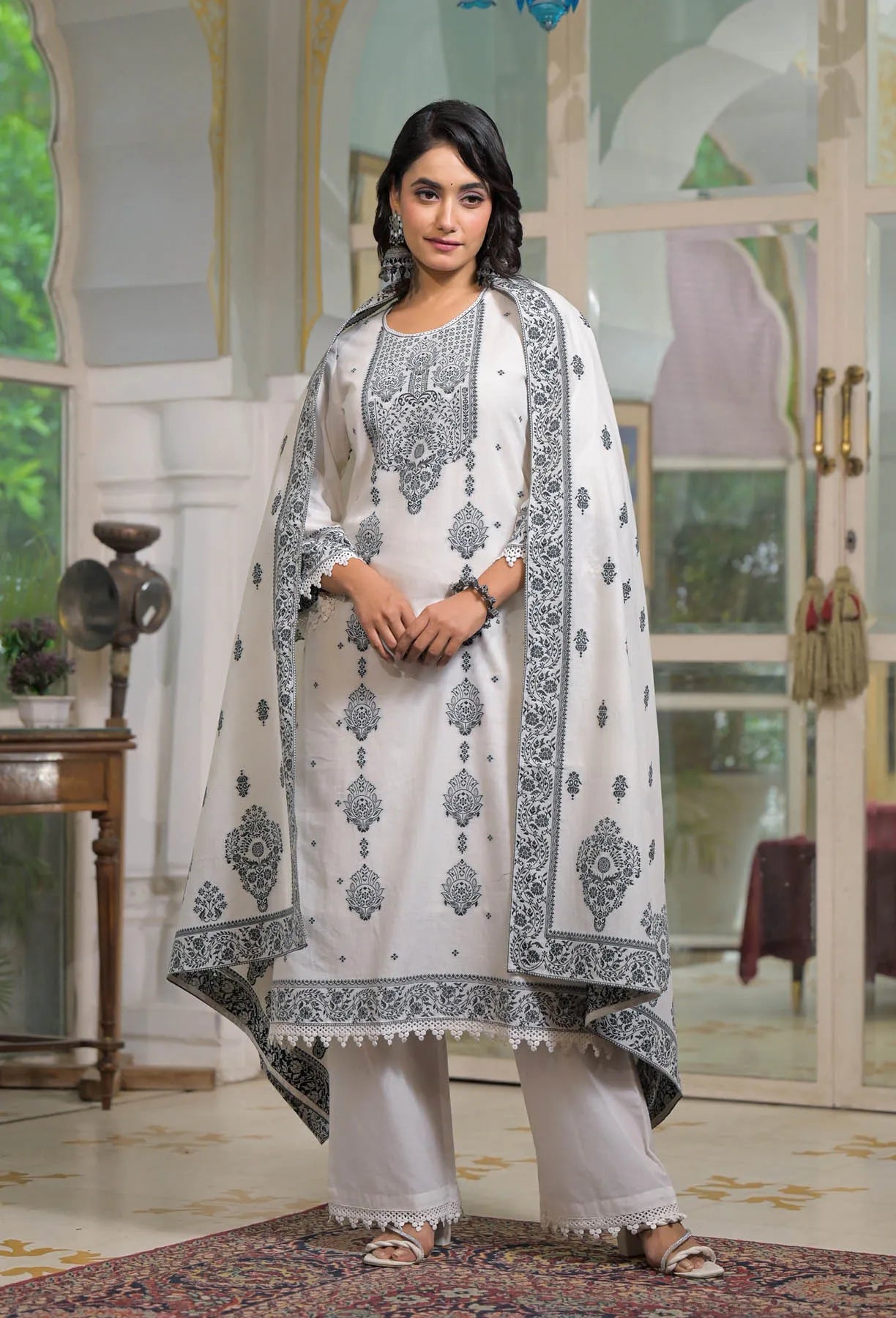 Woman wearing a white and black embroidered traditional outfit in an elegant room.