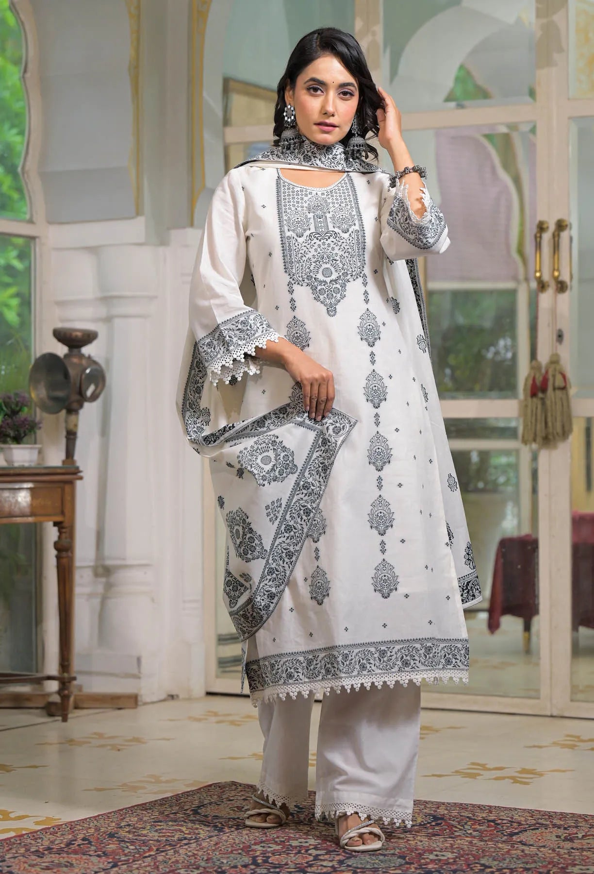 Woman wearing a white and black embroidered traditional outfit in a decorated room.