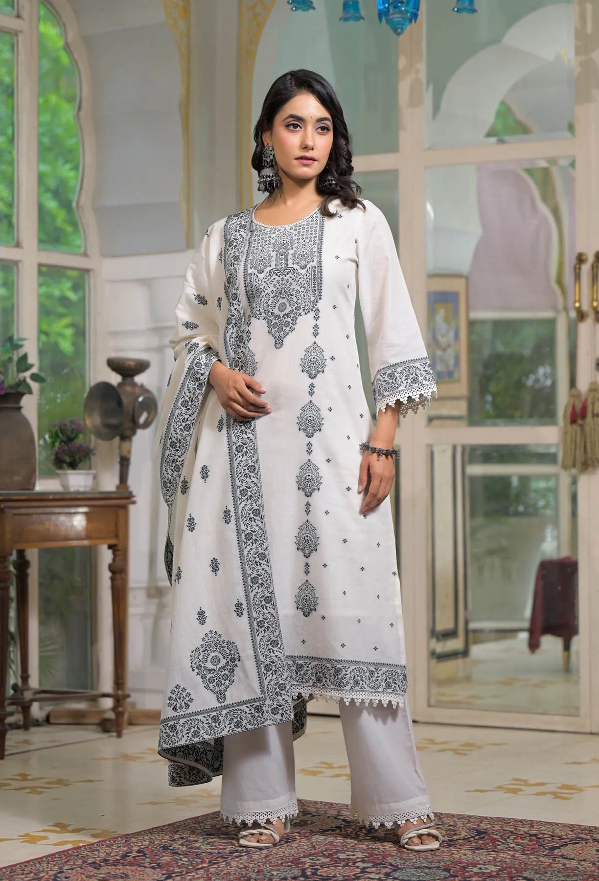 Woman wearing a white and black embroidered traditional outfit in an elegant room.