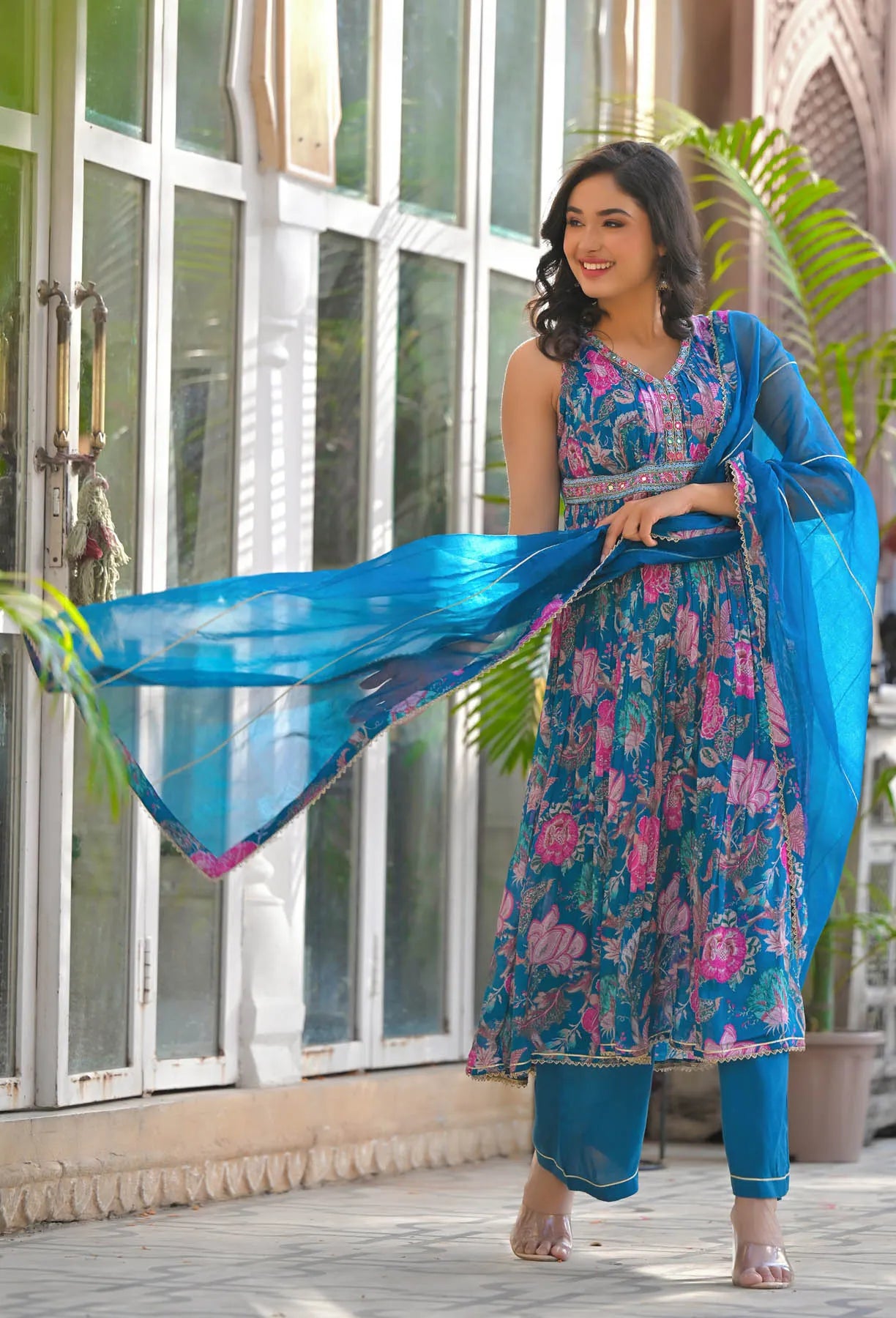 Woman in a blue and pink floral dress with a matching dupatta standing outdoors.