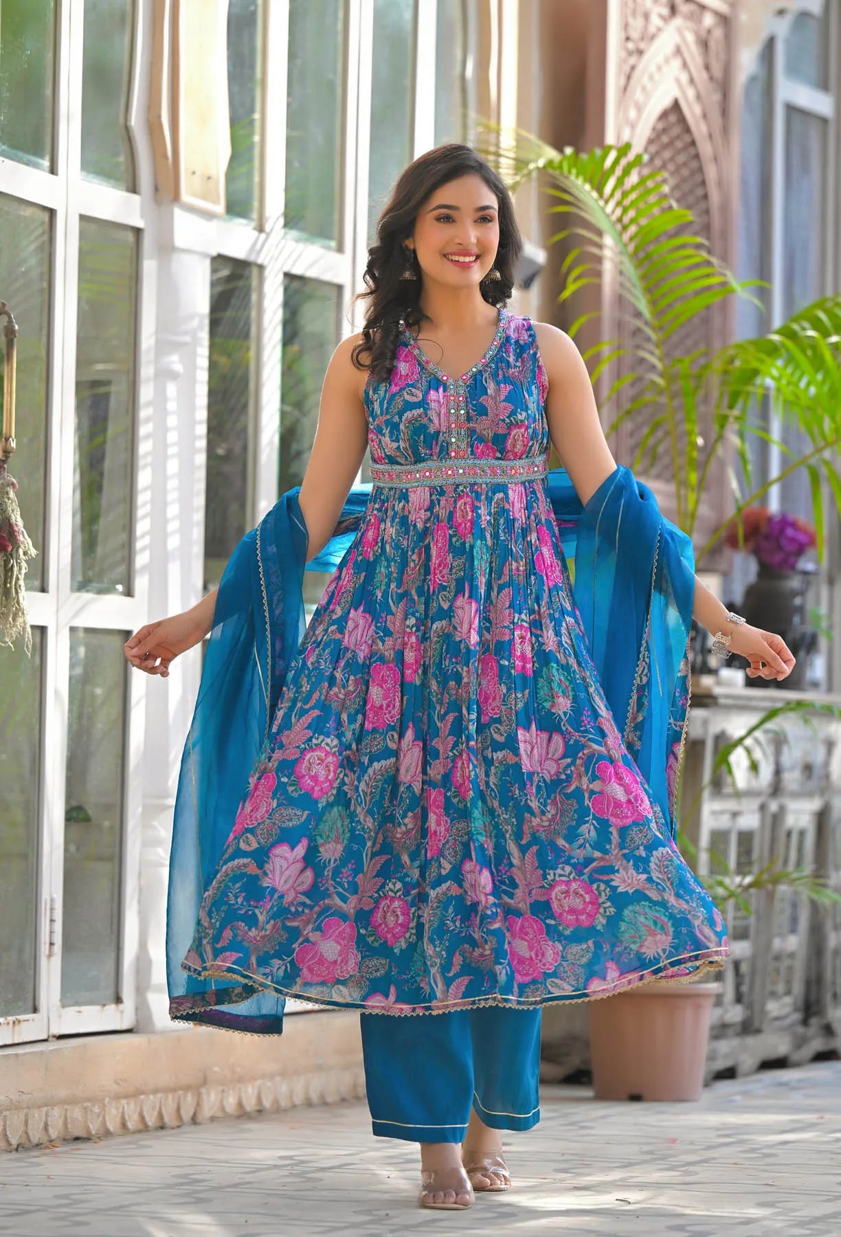 Woman wearing a blue and pink floral dress with a blue dupatta in an outdoor setting.