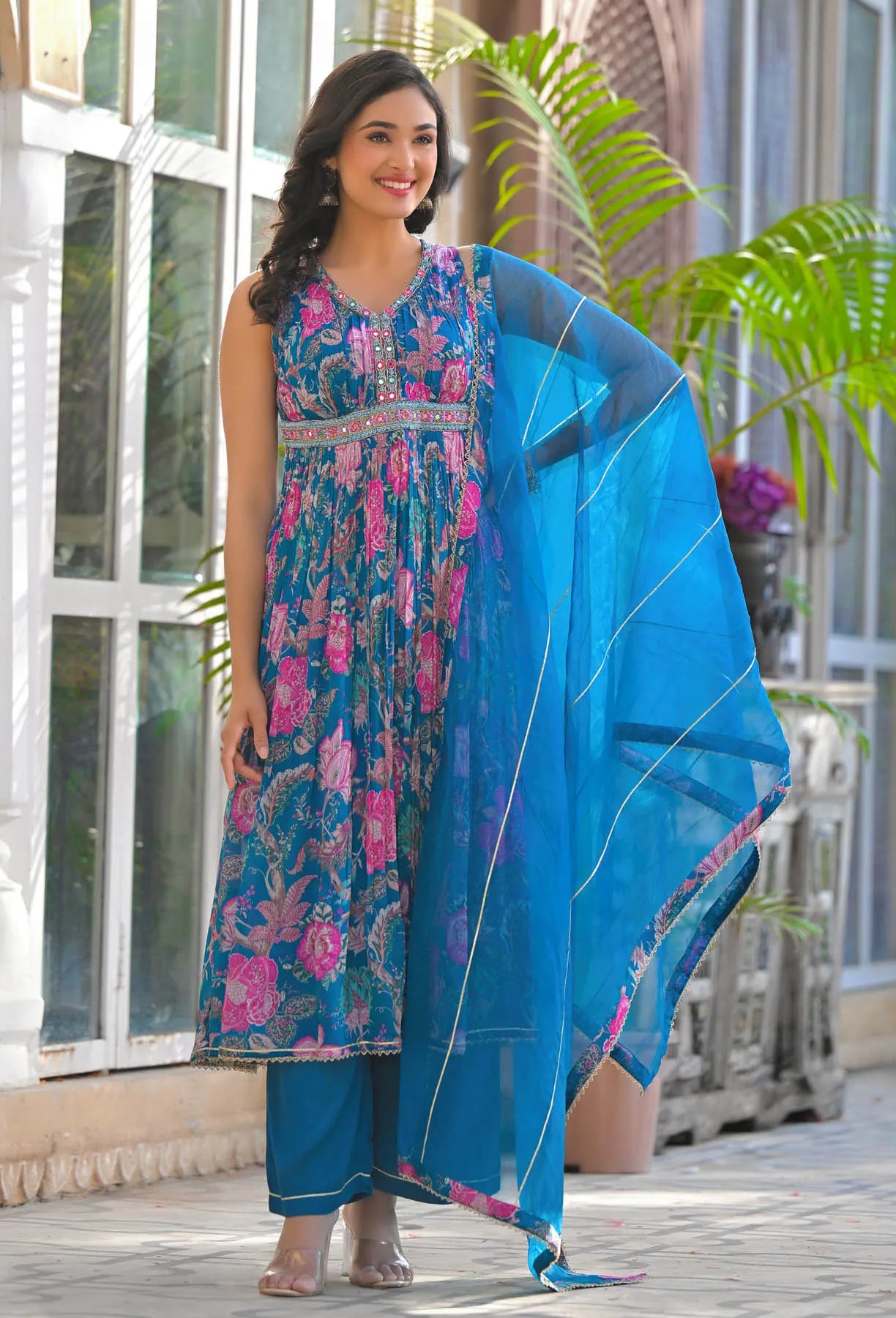Woman in a floral dress with a blue dupatta standing outdoors.