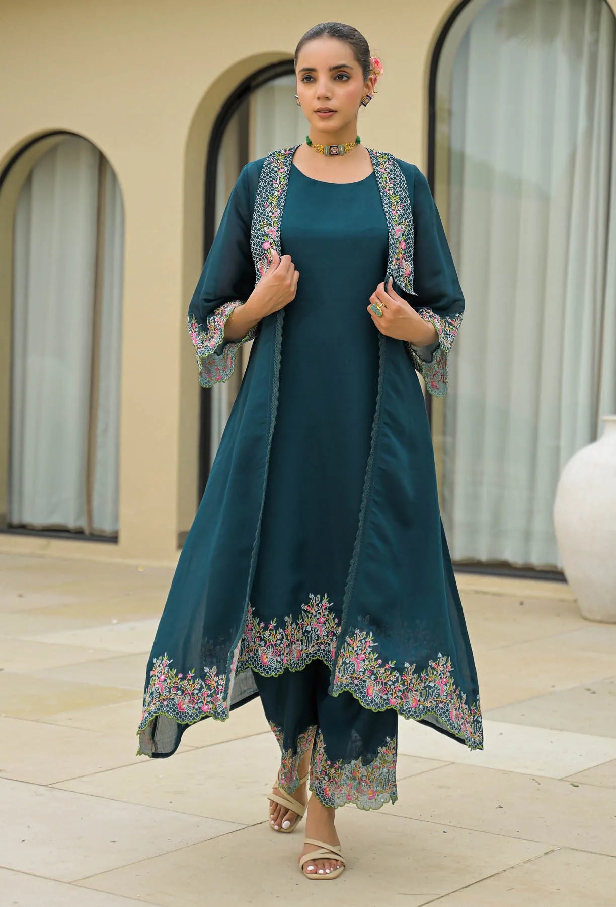 Woman wearing a teal outfit with floral embroidery in an outdoor setting