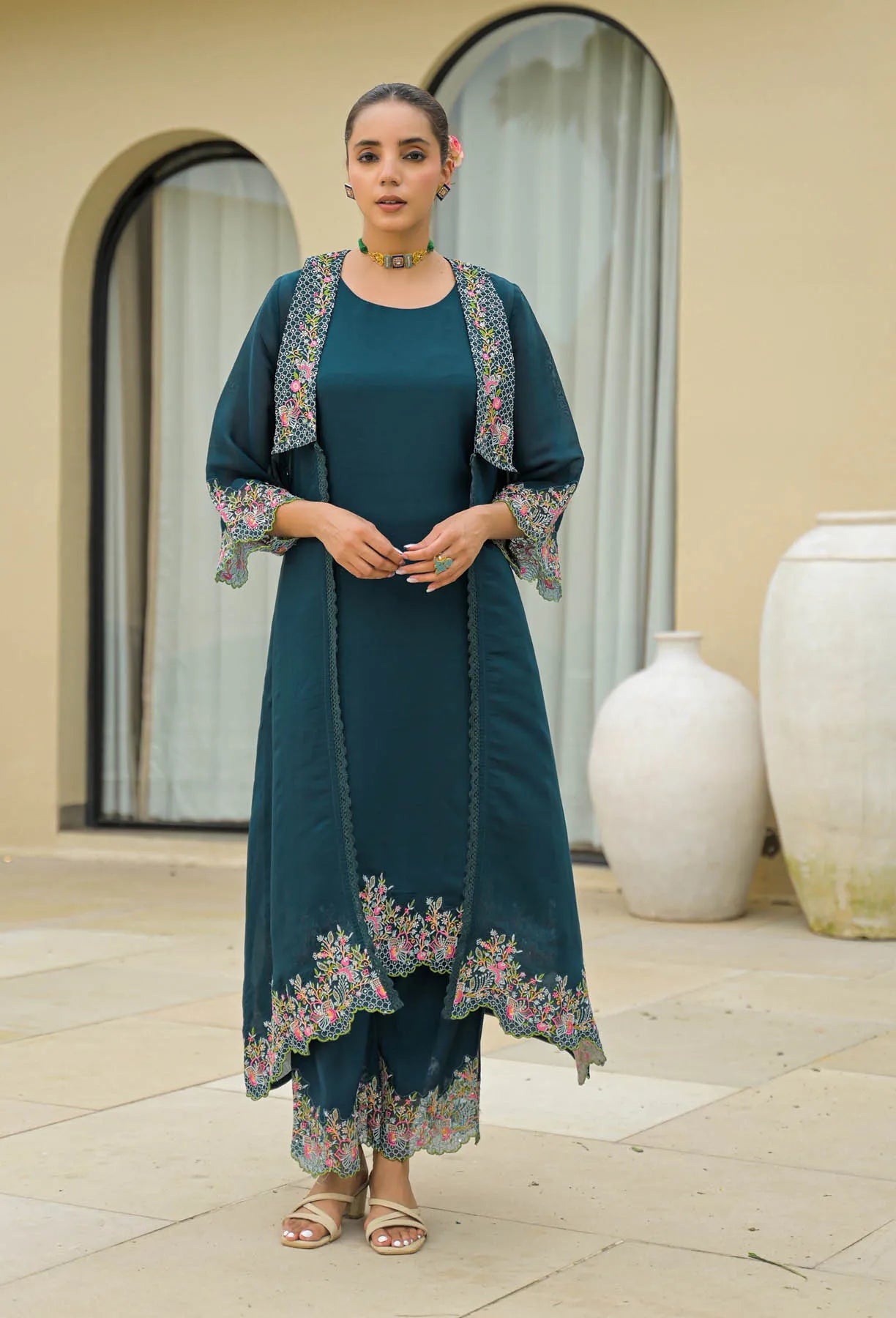 Woman wearing a teal outfit with floral embroidery standing outdoors.