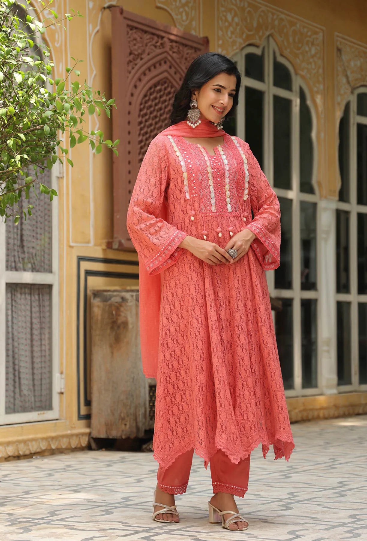 Woman in a coral pink traditional outfit standing in front of an ornate building.