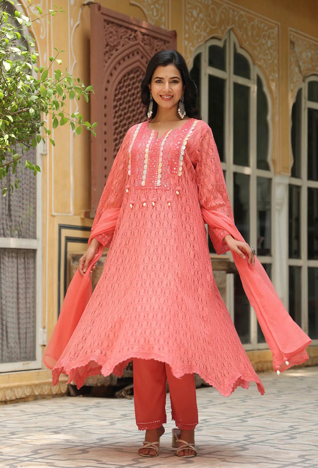 Woman wearing a pink traditional outfit with intricate designs in an outdoor setting.