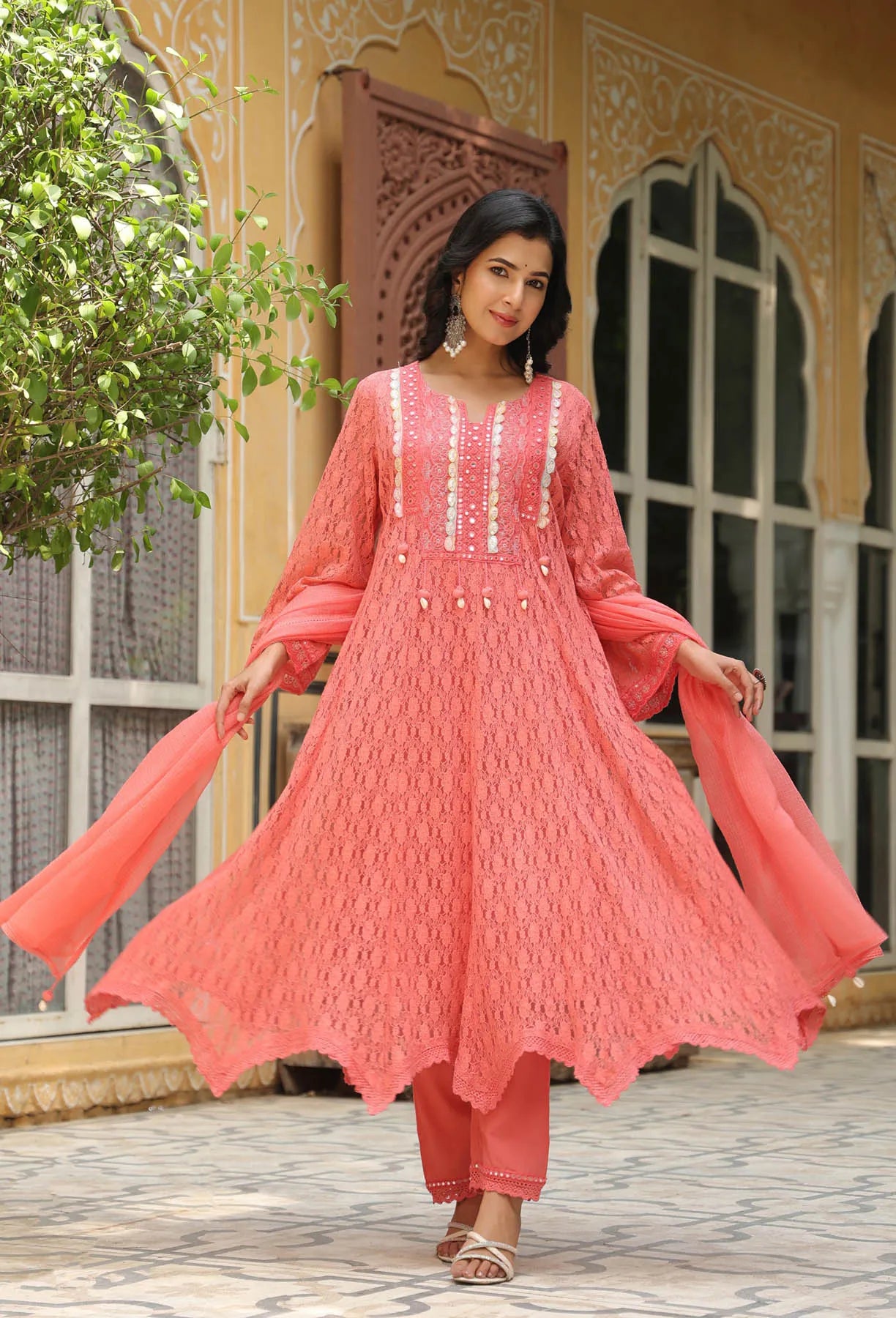 Woman in a pink traditional outfit standing outdoors with decorative architecture in the background