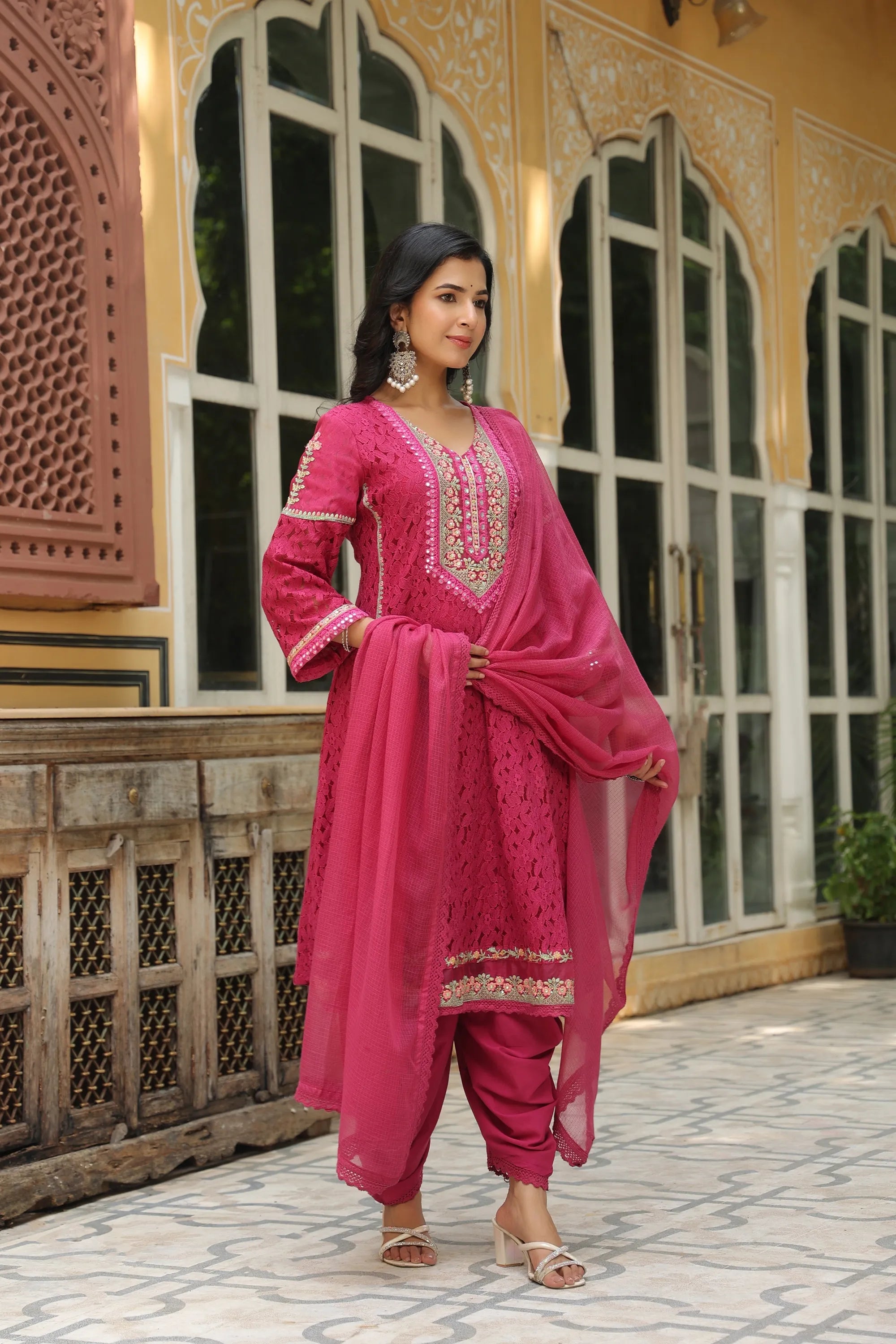 Woman in a pink traditional outfit standing in front of decorative architecture.