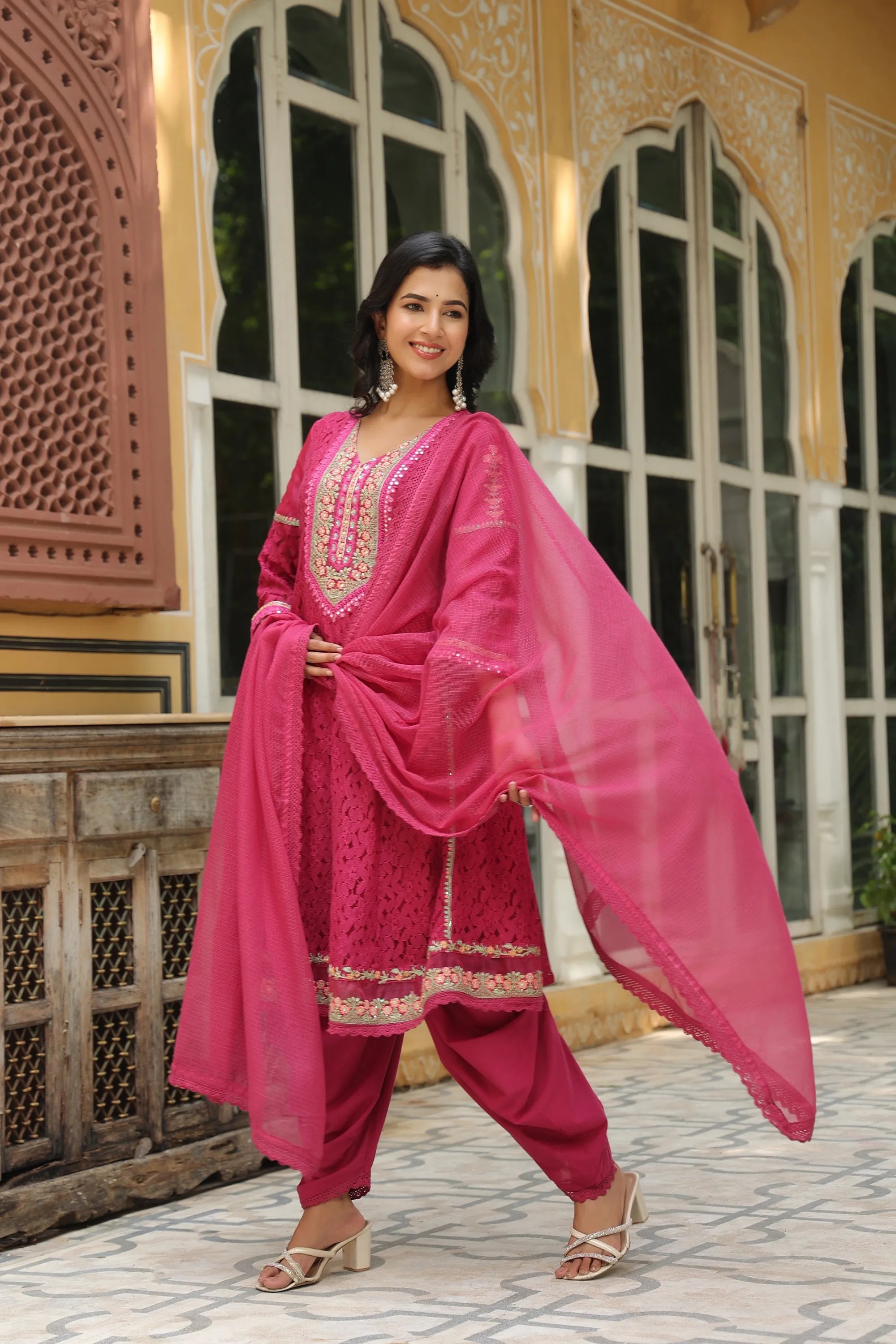 Woman in a bright pink traditional outfit standing in front of an ornate building.