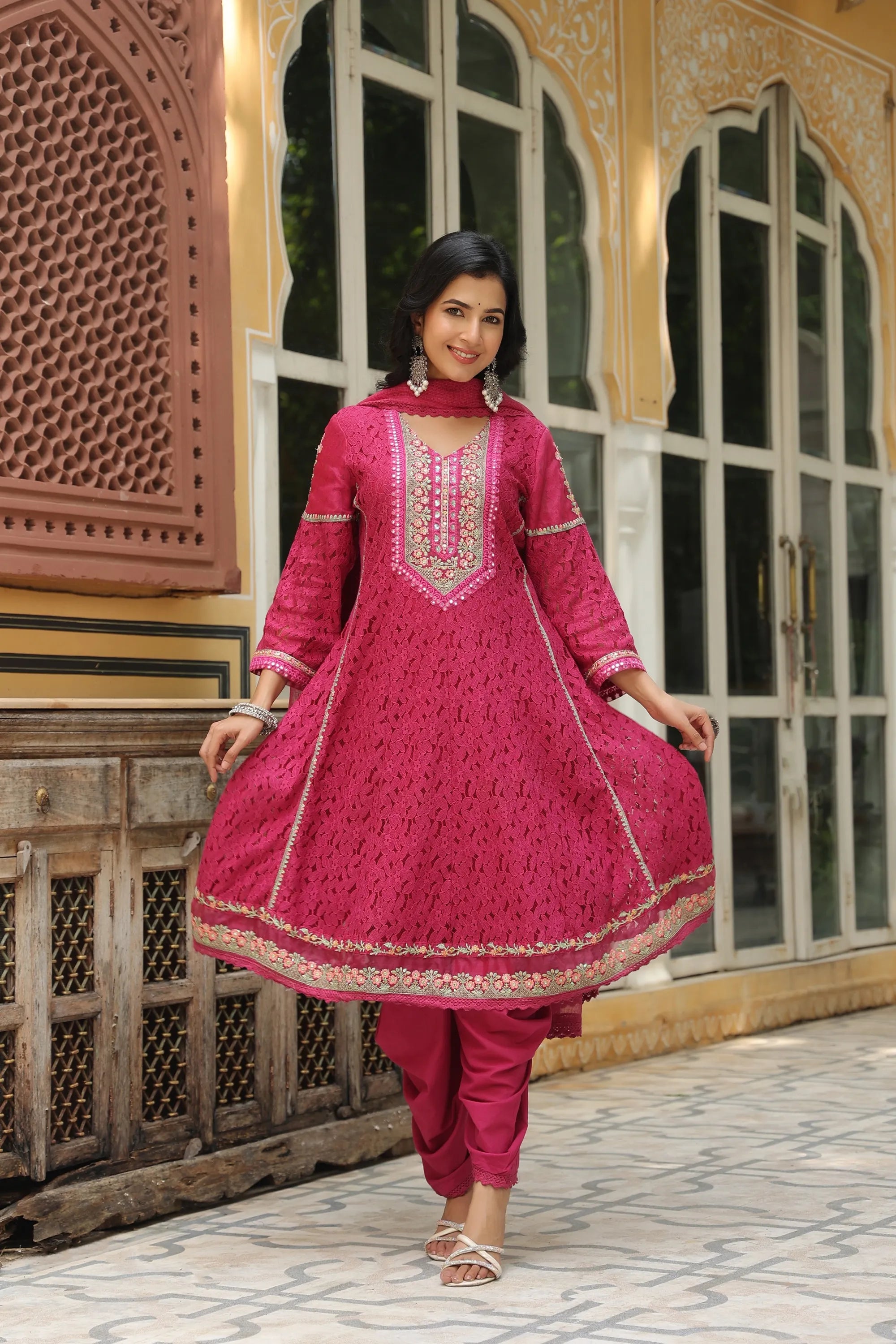 Woman in a pink traditional outfit standing in front of decorative architecture.