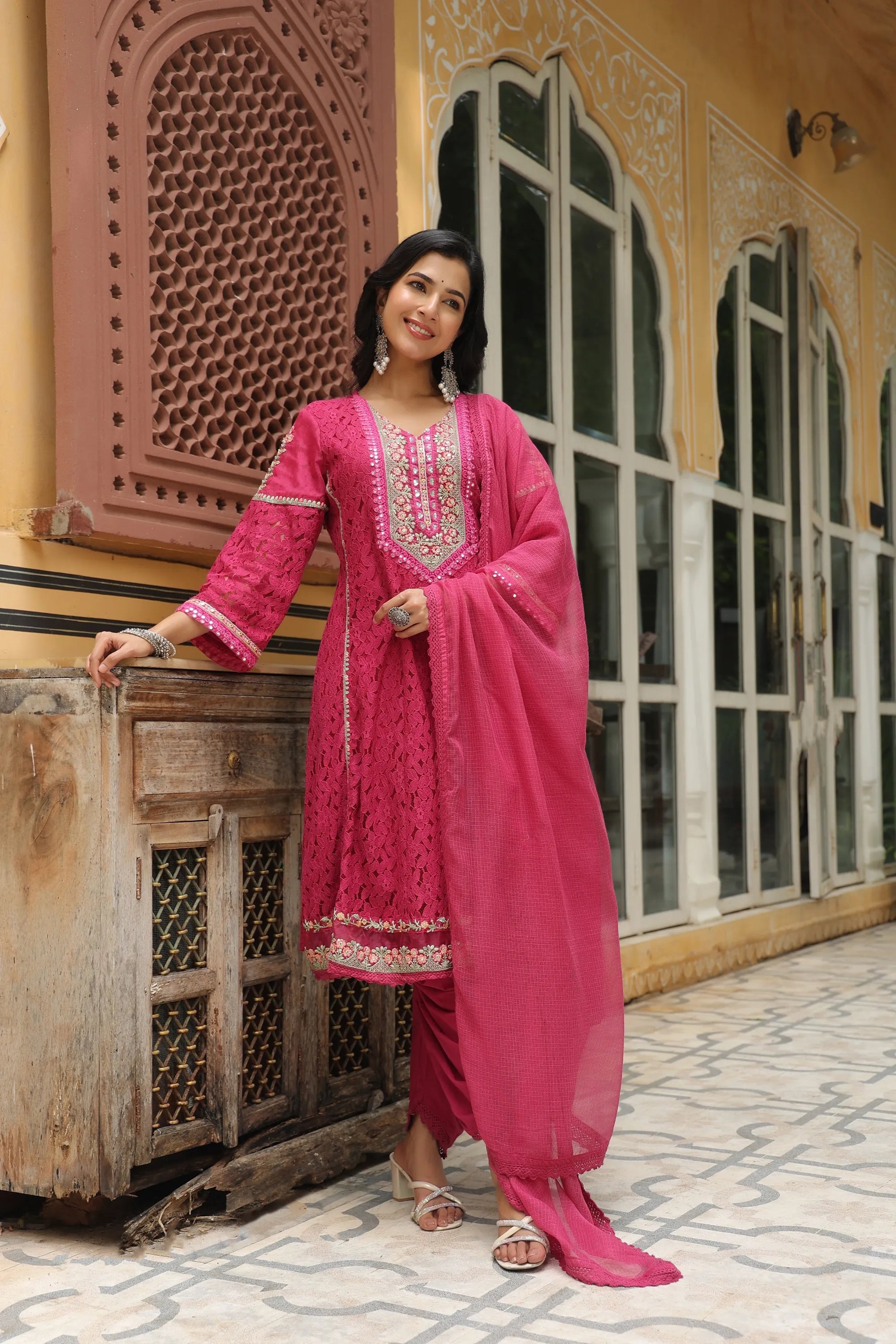 Woman in a pink traditional outfit standing in front of a decorative wall.