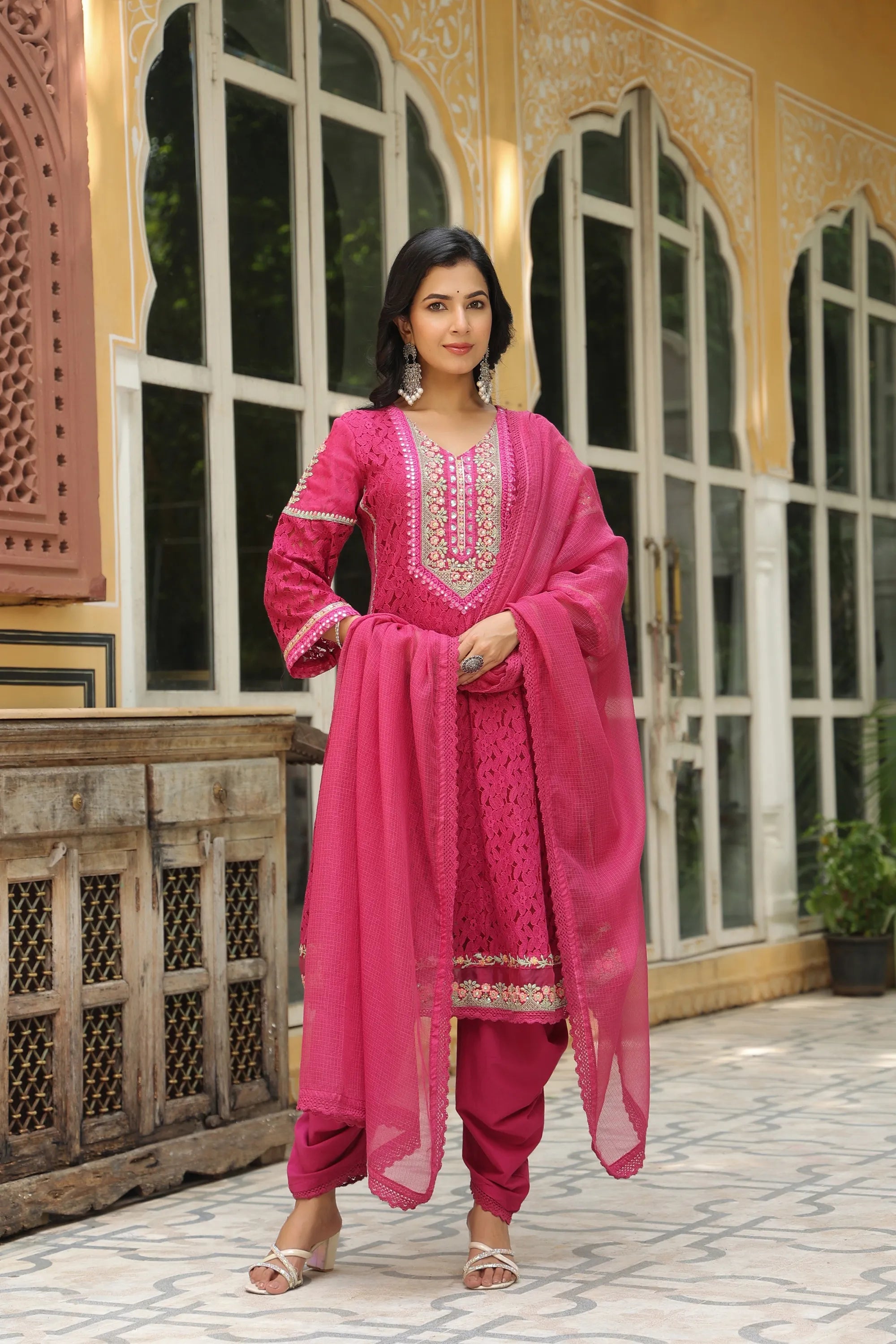 Woman in a pink traditional outfit standing in front of an ornate building.