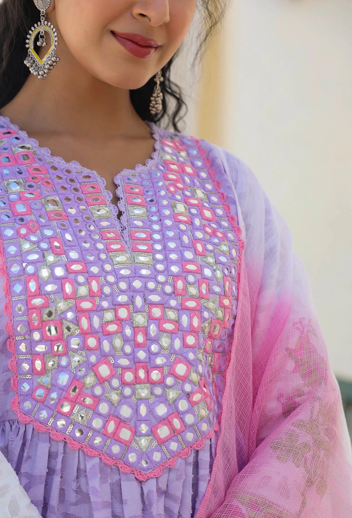 Close-up of a person wearing a purple and pink embroidered traditional outfit with a blurred background.