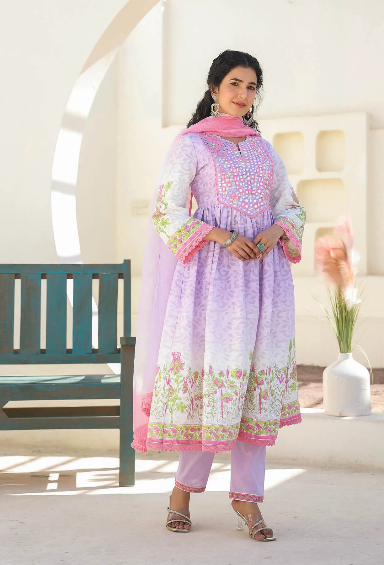 Woman wearing a light purple traditional outfit with floral patterns in a bright, minimalistic setting.