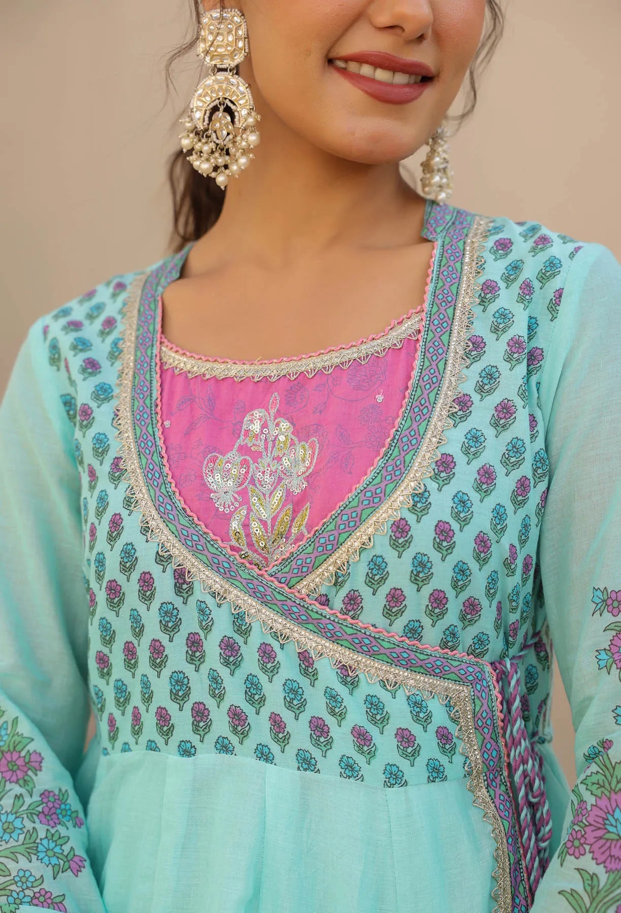 Woman wearing a light blue and pink embroidered traditional outfit with earrings.