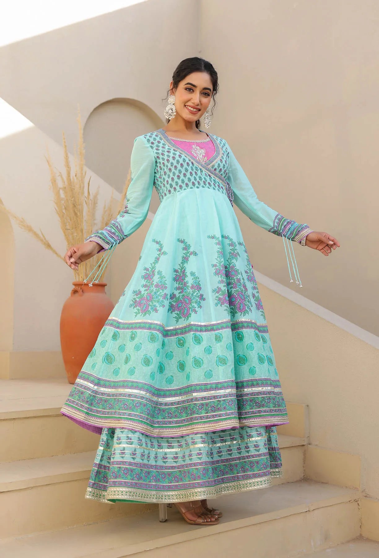 Woman in a light blue traditional outfit standing on steps with a neutral background