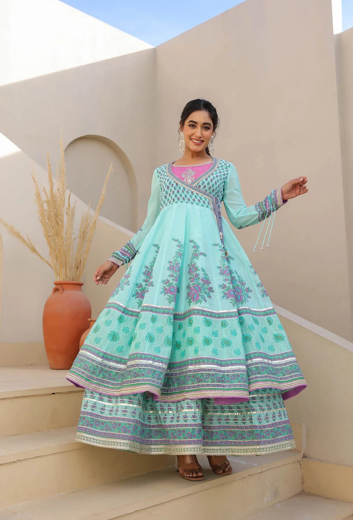 Woman in a light blue embroidered traditional outfit standing on steps with a neutral background