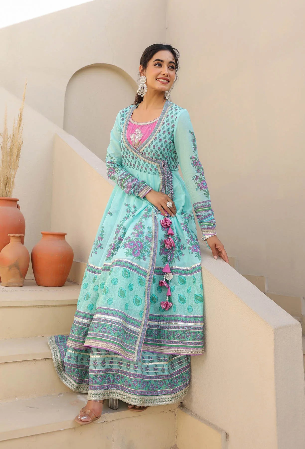 Woman in a traditional outfit standing on steps with decorative vases in the background